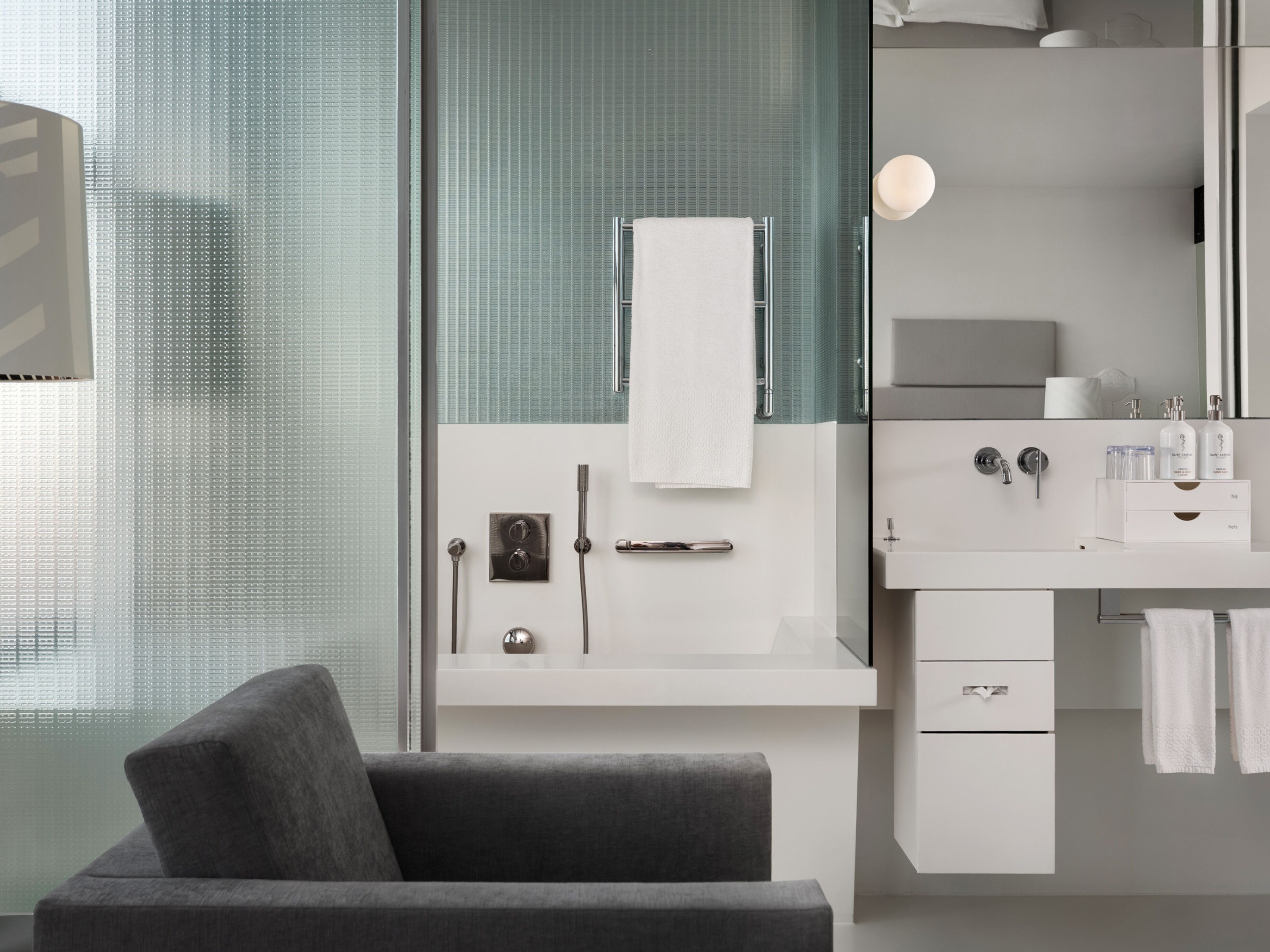 A modern bathroom with a glass shower enclosure, a white vanity, and a grey sofa.