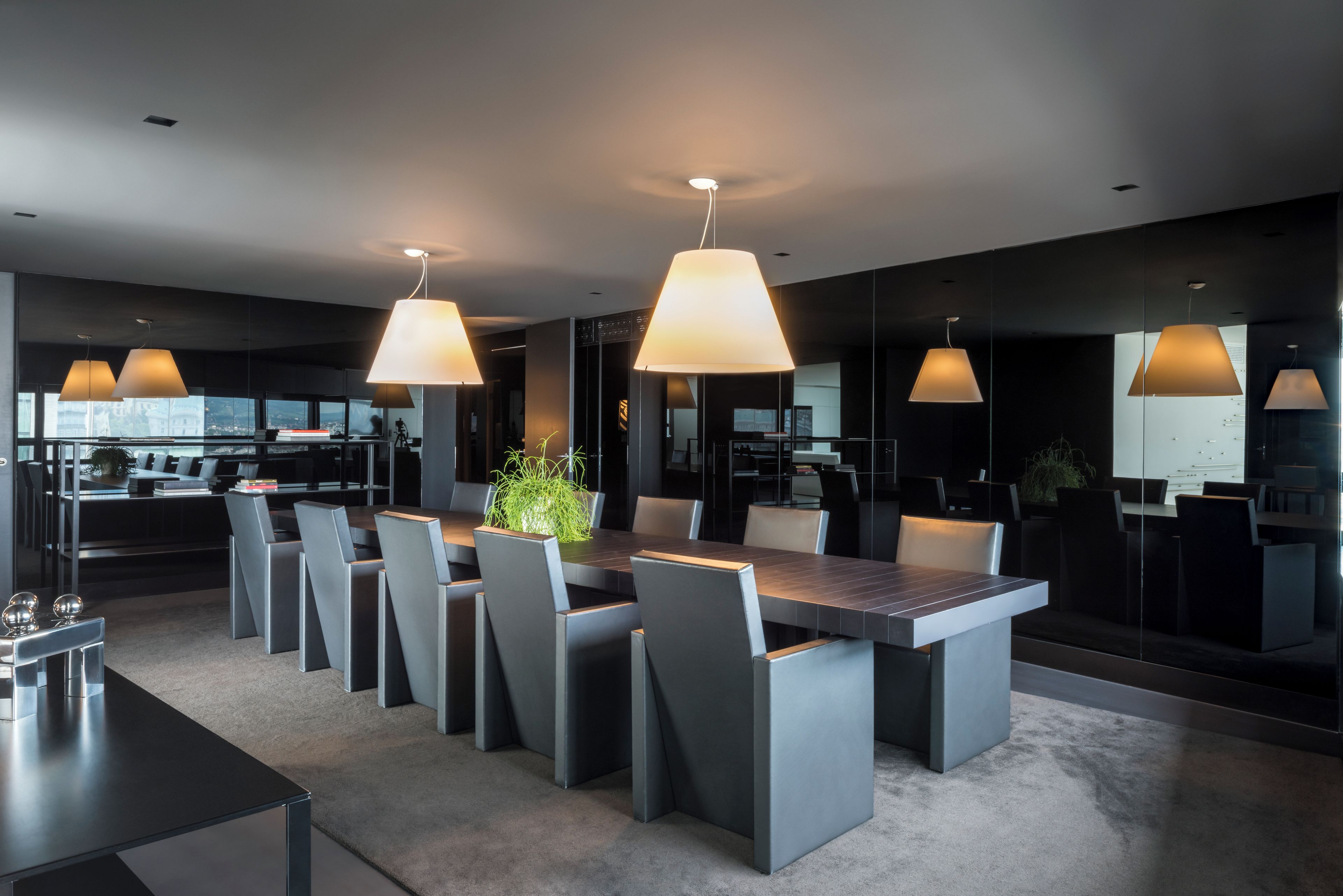 Uma área de jantar moderna com uma mesa retangular grande, várias cadeiras e iluminação pendente.