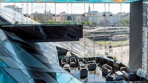 Un interior moderno con un muro de cristal que ofrece vistas a la ciudad, un televisor suspendido y un mobiliario contemporáneo.