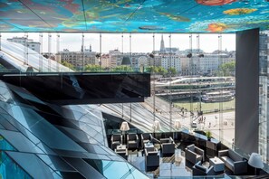 Ein modernes Interieur mit Glaswand und Blick auf die Stadt, einem hängenden Fernseher und moderner Sitzgelegenheit.
