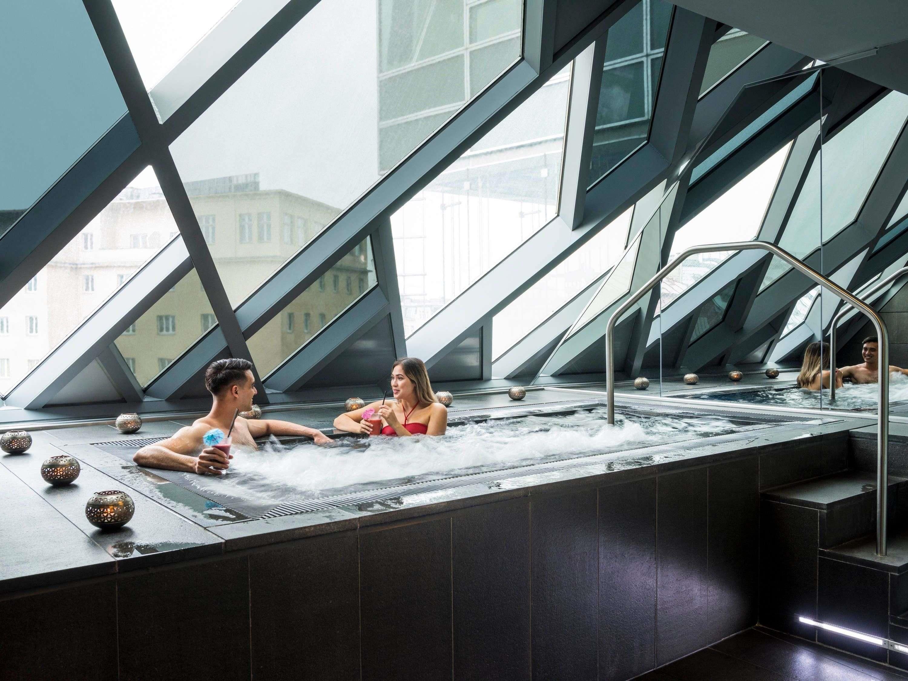 A modern spa with a glass-enclosed hot tub area, geometric architectural design, and a view of buildings outside.
