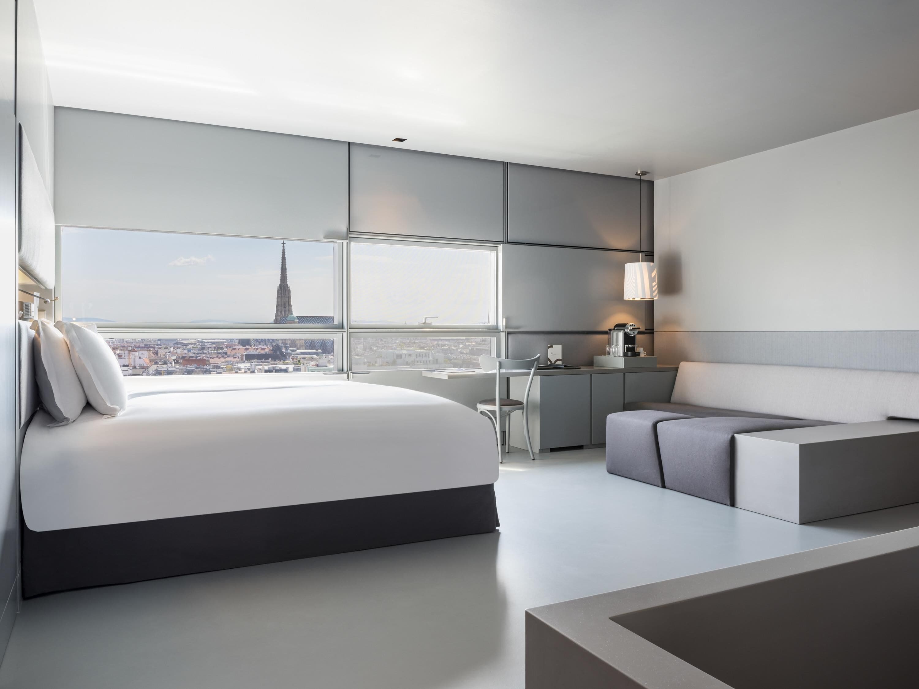 Quarto de hotel moderno com uma cama grande, uma escrivaninha, uma cadeira e um sofá.