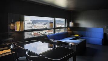 Quarto moderno com mesa de jantar, cadeiras, um sofá azul e vista da cidade através de grandes janelas.