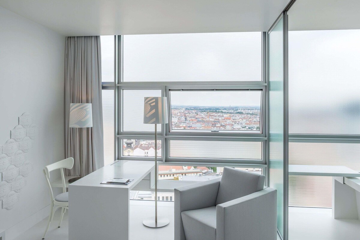 A modern room with a large window, a desk, two chairs, and a lamp.