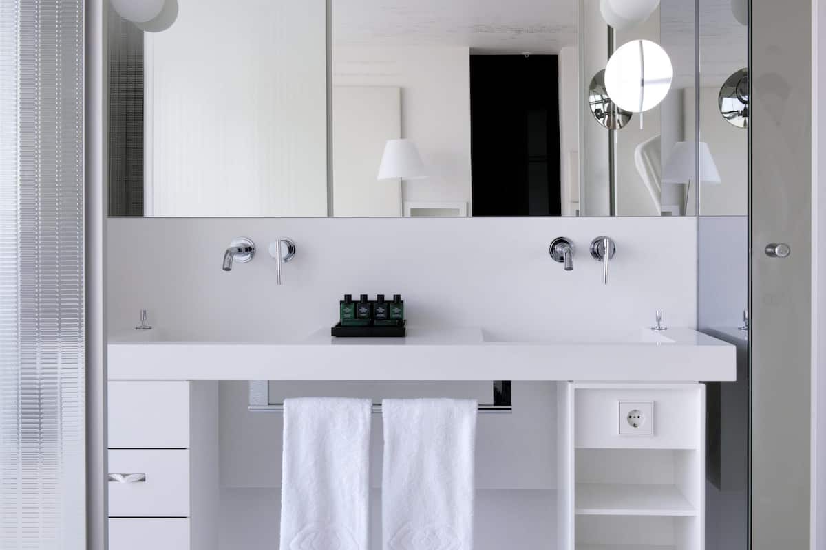 Ein modernes Badezimmer mit einem weißen Waschtisch, zwei Waschbecken, einem großen Spiegel und einem Handtuchhalter.