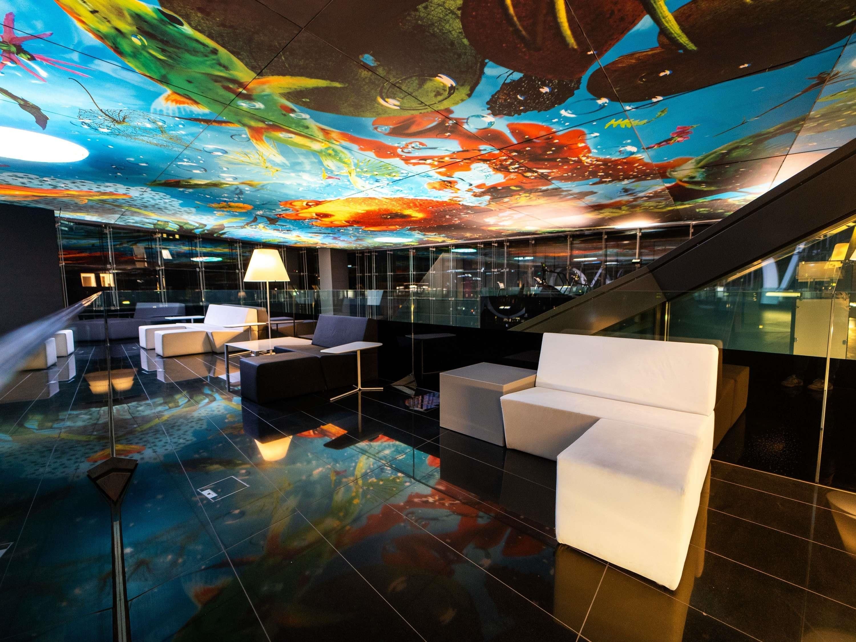 A modern lobby with a digital ceiling display, seating areas, and a glass railing.