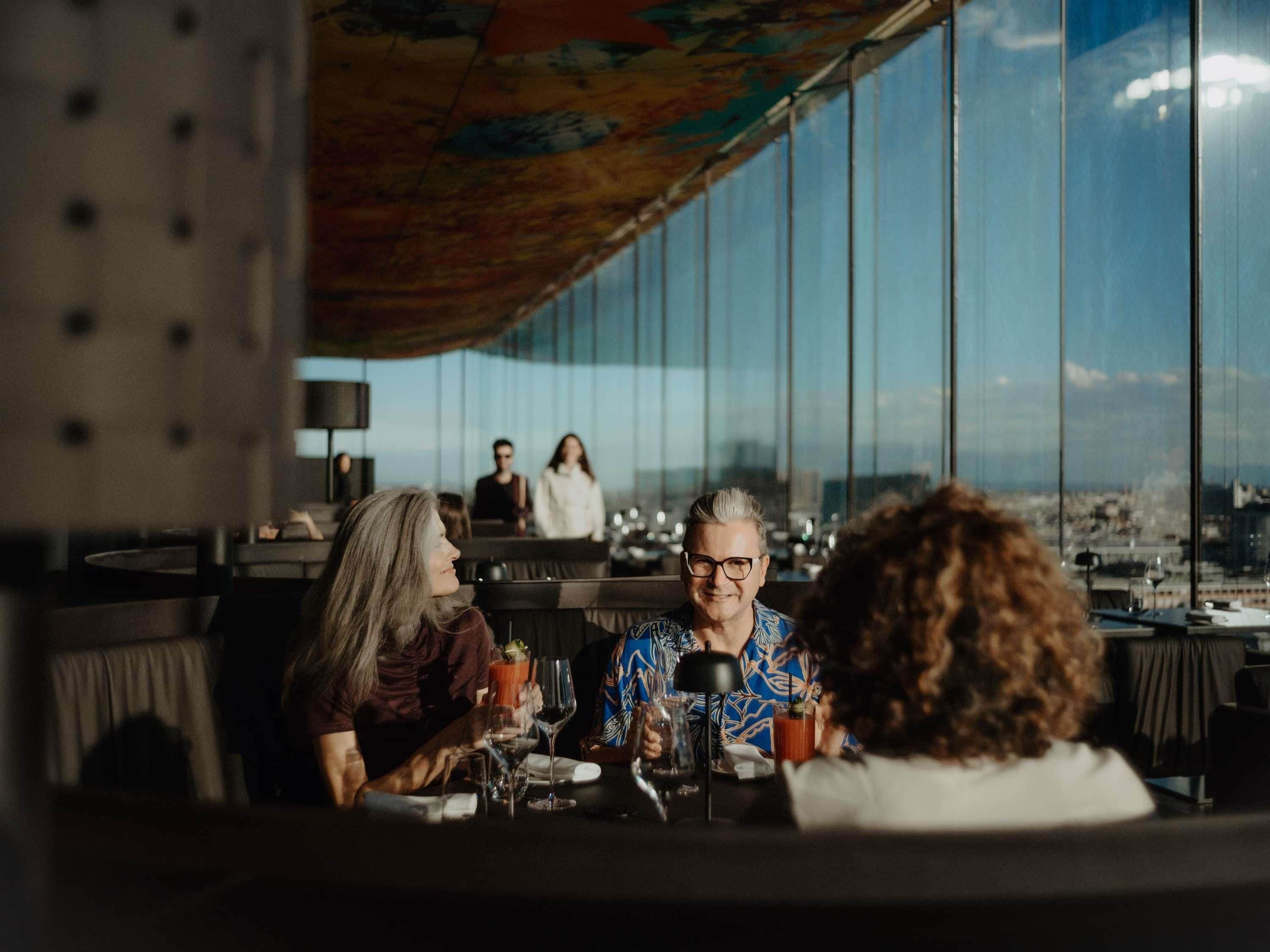 Restaurante com amplas janelas que oferecem vista da cidade, mesas preparadas para refeições e teto com design de mapa.