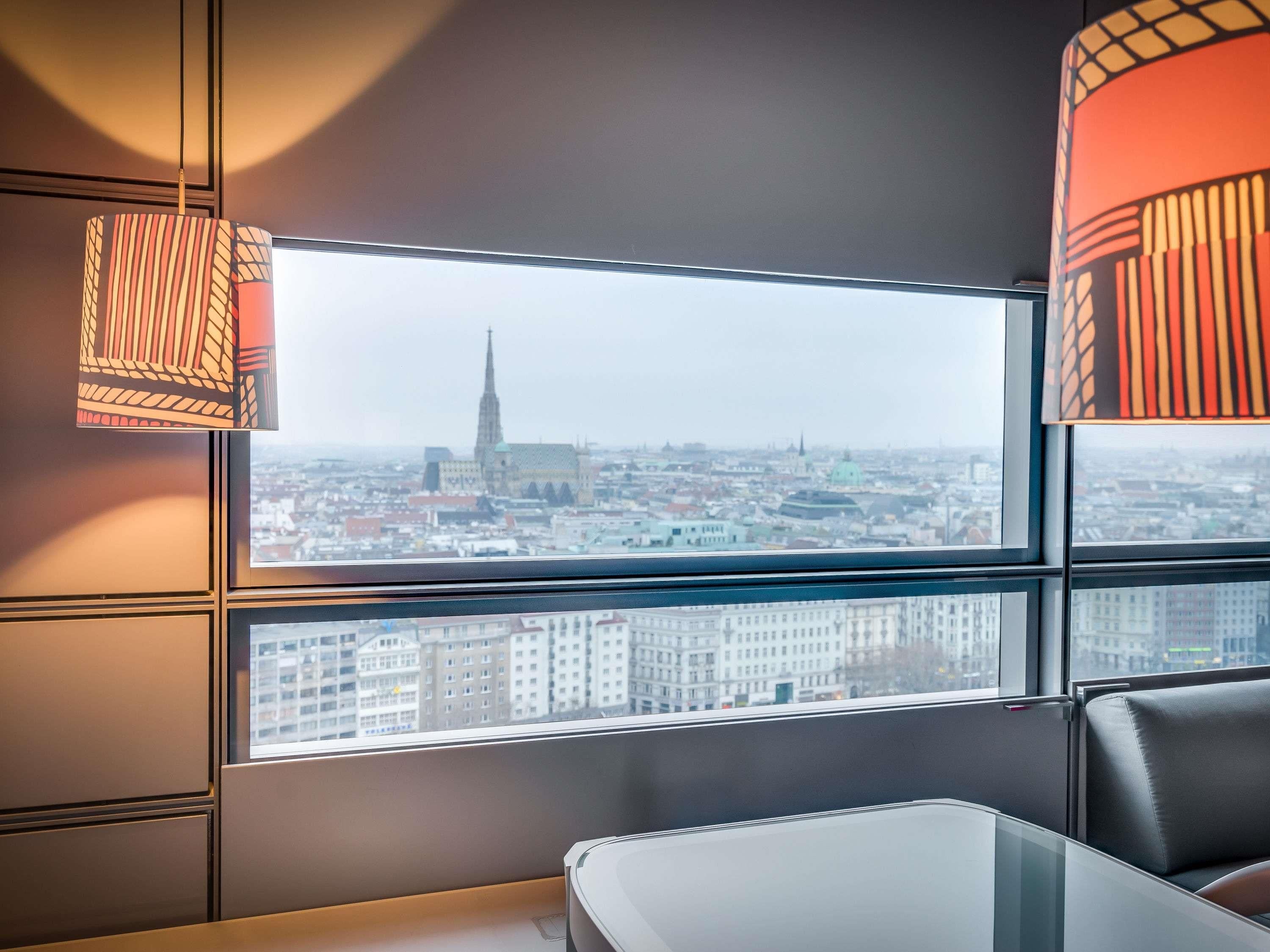 A modern room with a large window, a table, and a chair, overlooking a cityscape with a prominent church spire.