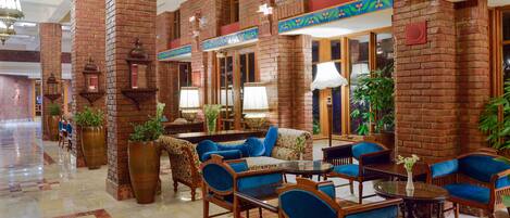 A lobby with brick walls, blue upholstered furniture, and large potted plants.