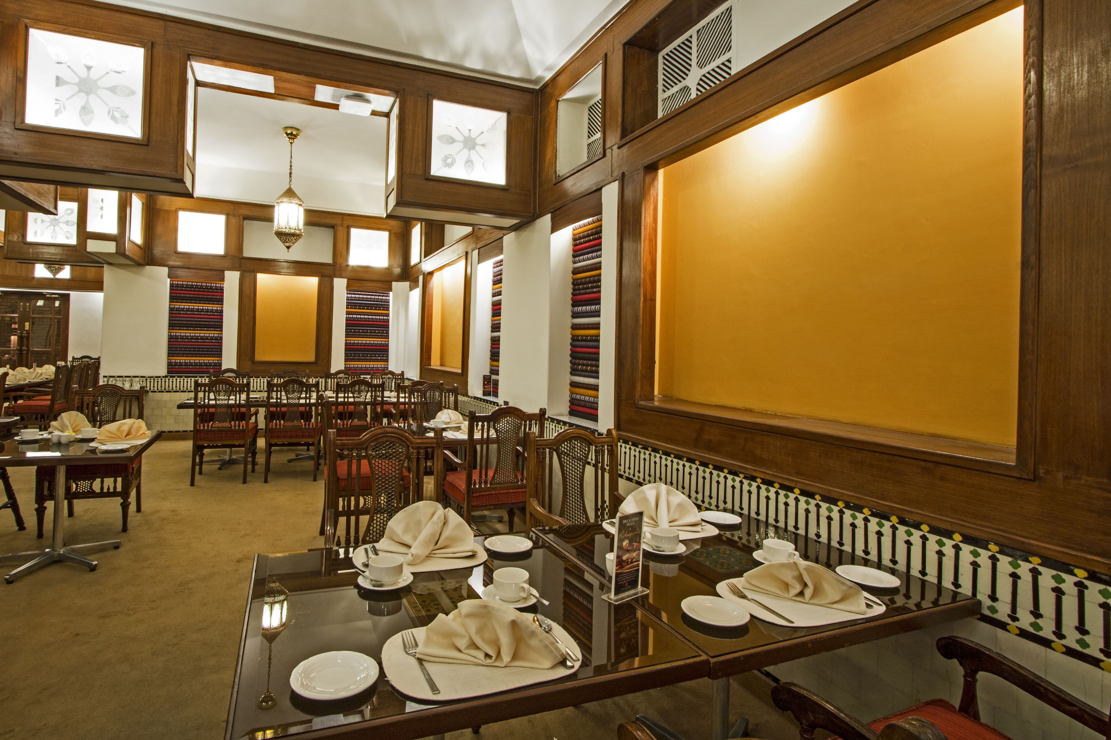 A dining area with multiple tables set for service, wooden paneling, and a large window with a view.