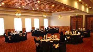 Un salón de banquetes con varias mesas redondas dispuestas para eventos, con manteles negros y sillas adornadas con cintas doradas.
