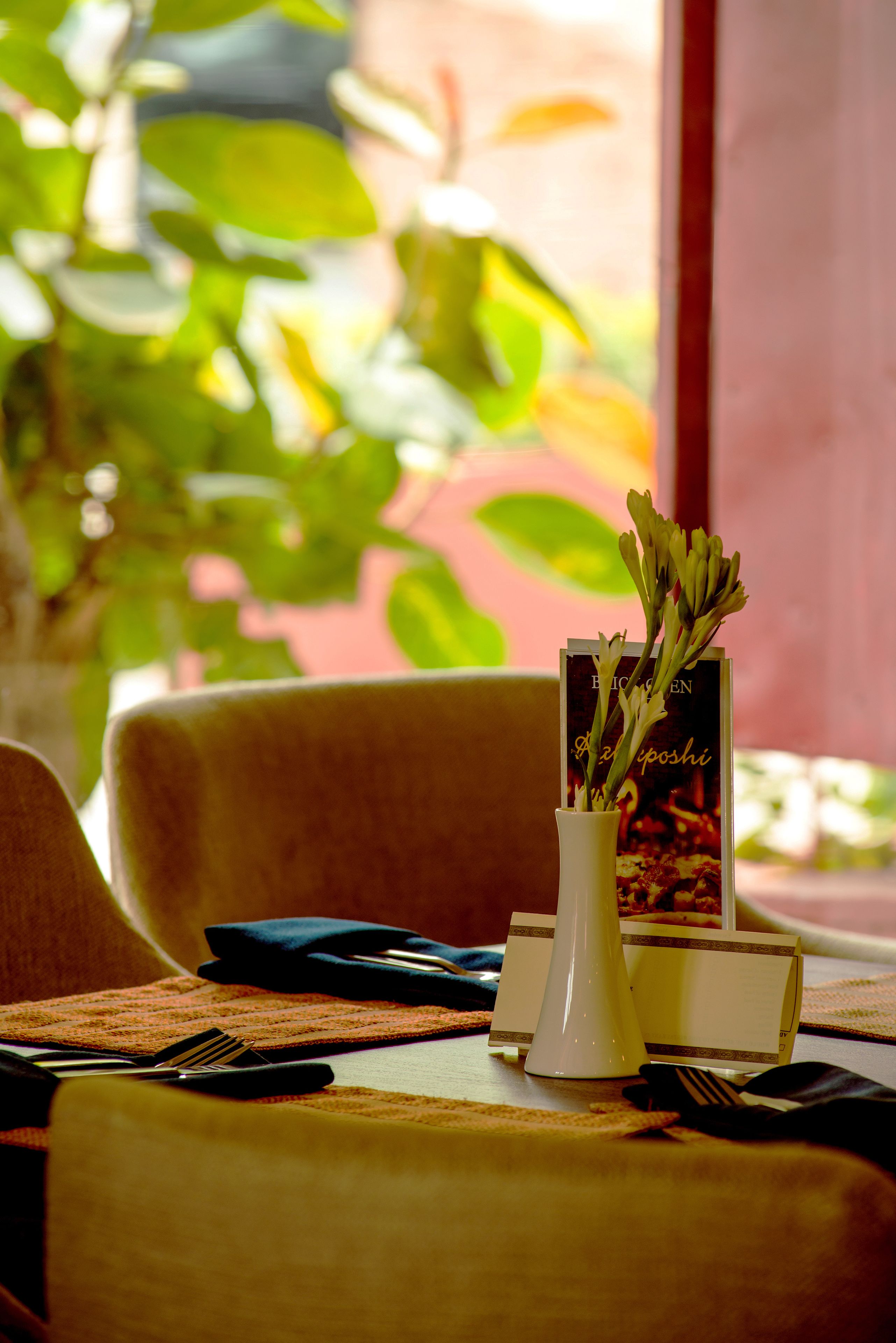 A dining table with a vase of flowers, a menu, and cutlery.