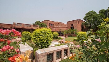 A courtyard with brick buildings, a central green bush, and flowering plants.