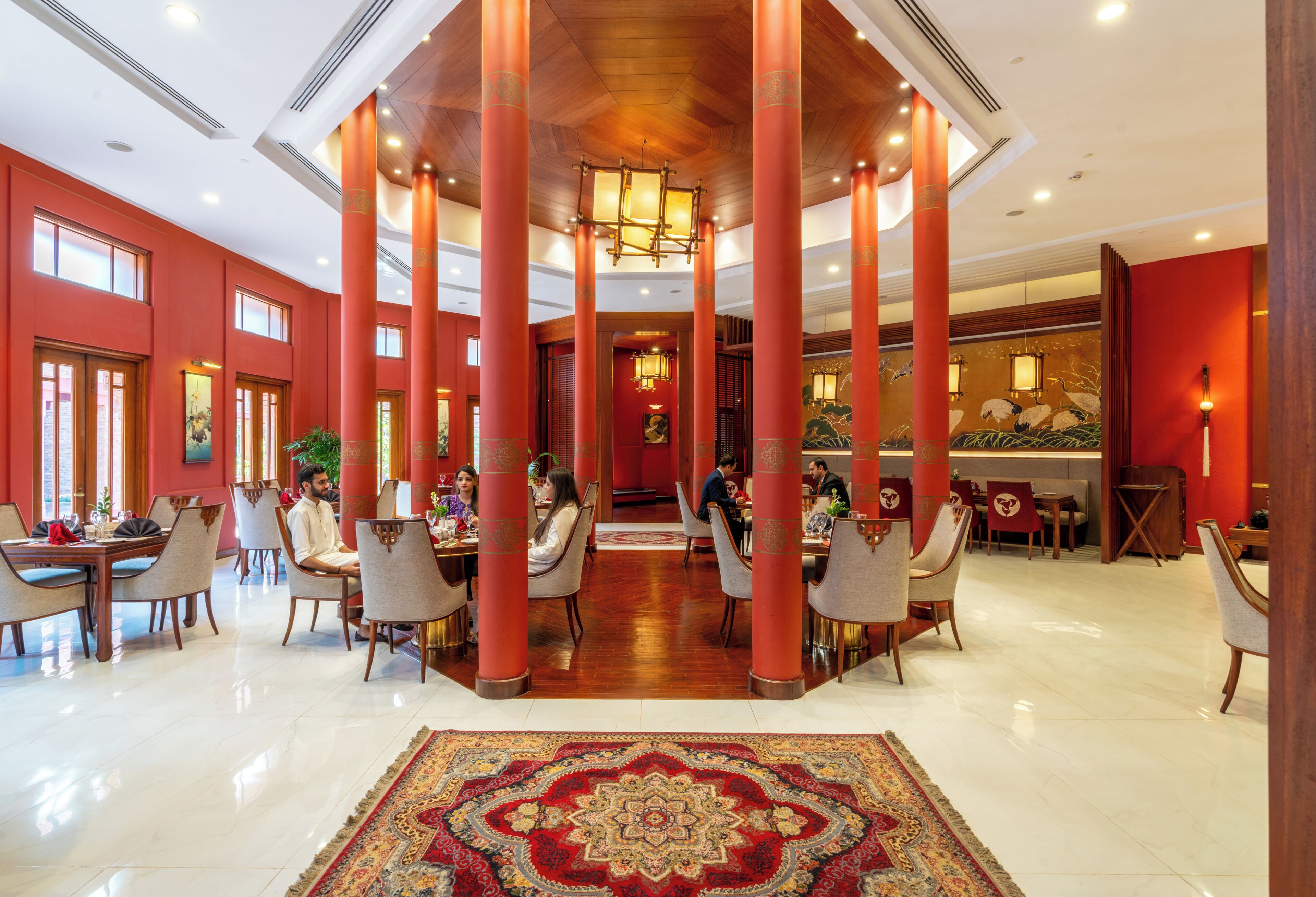 A spacious lobby with high ceilings, red pillars, and a central chandelier.
