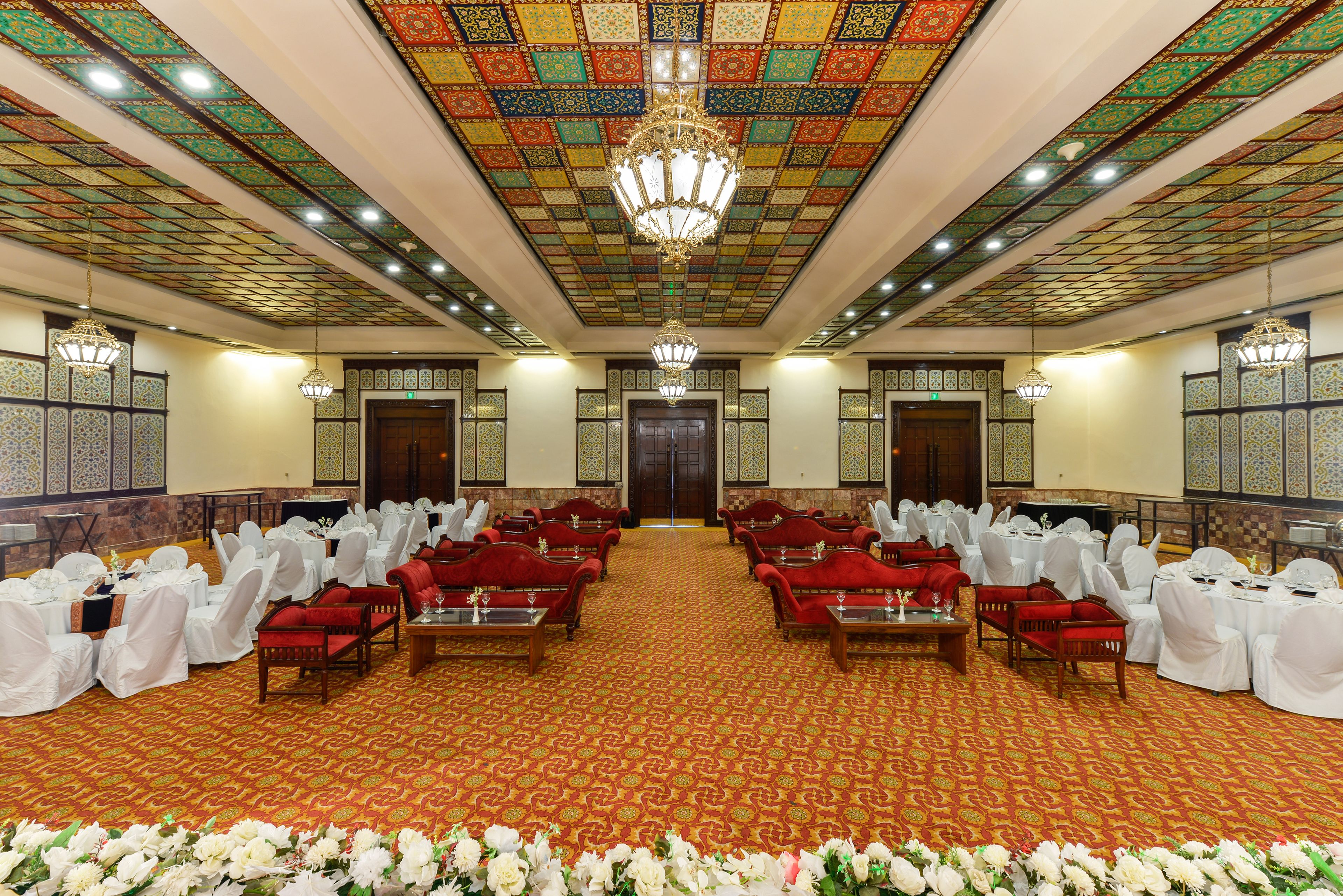 Une salle de banquet avec des rangées de tables et de chaises, une moquette à motifs et un lustre.