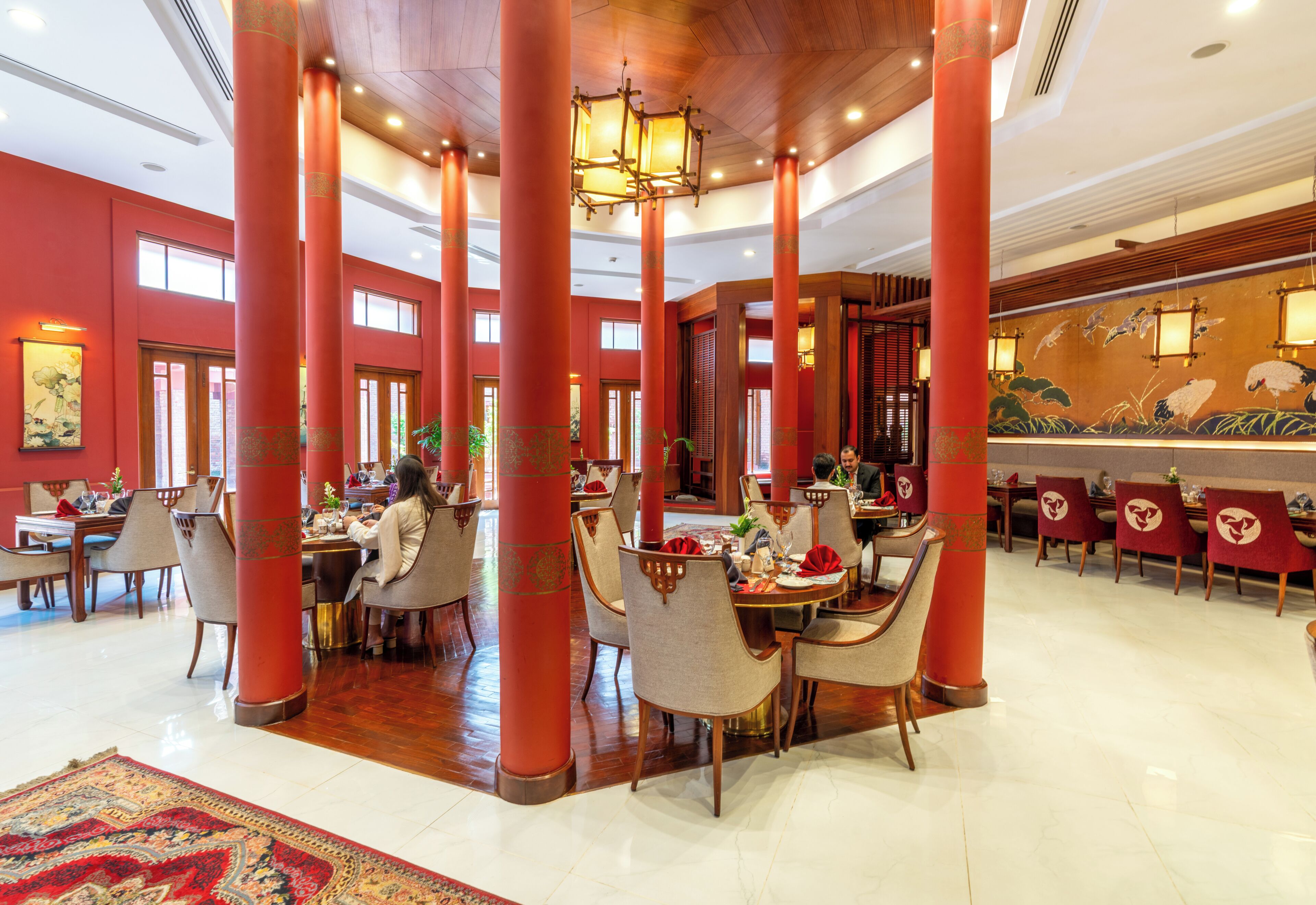Un hall d’hôtel spacieux, doté de hauts plafonds, de piliers rouges et d’un décor traditionnel.
