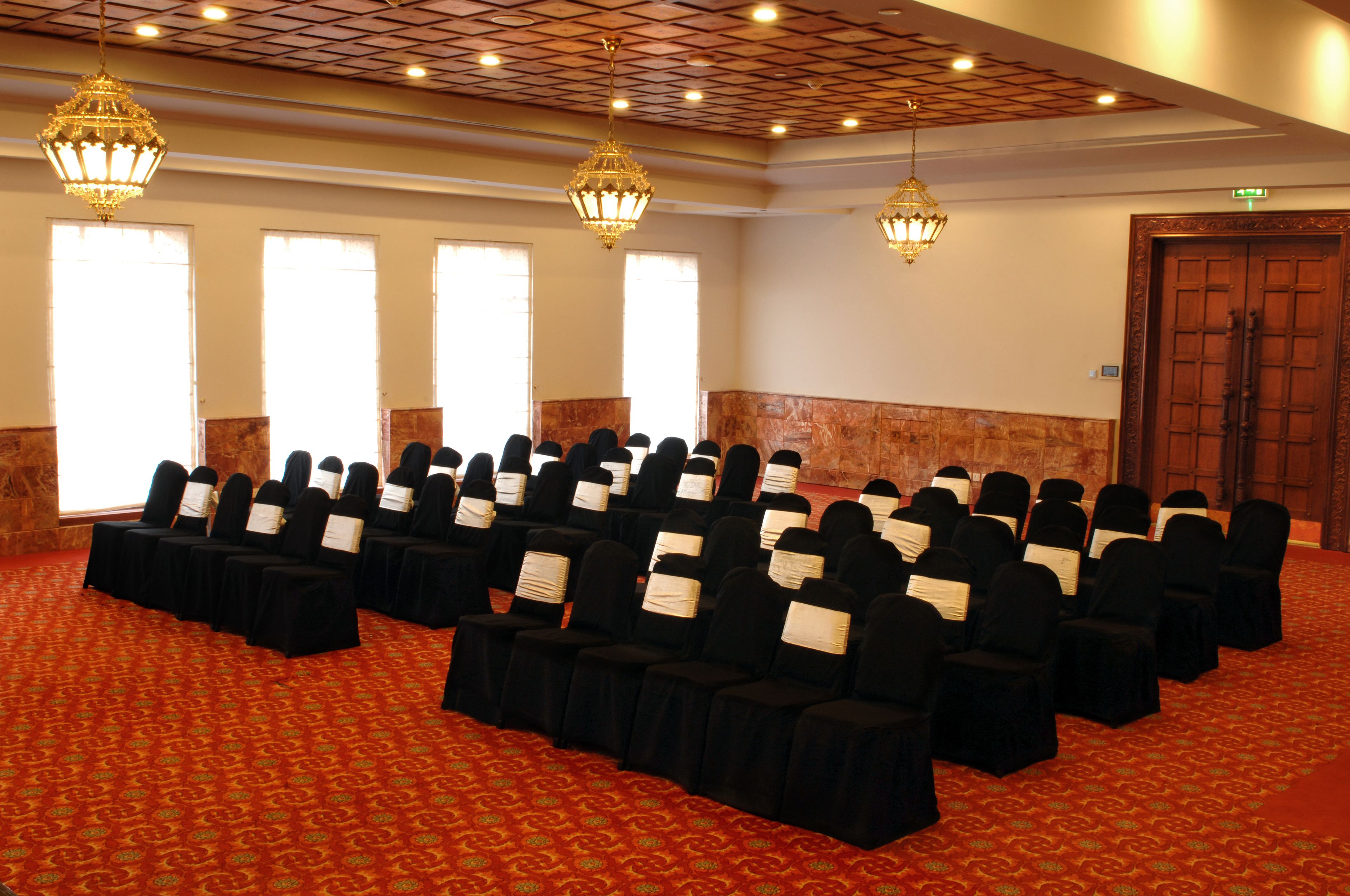 Un salón de conferencias con filas de sillas, candelabros y una alfombra estampada.