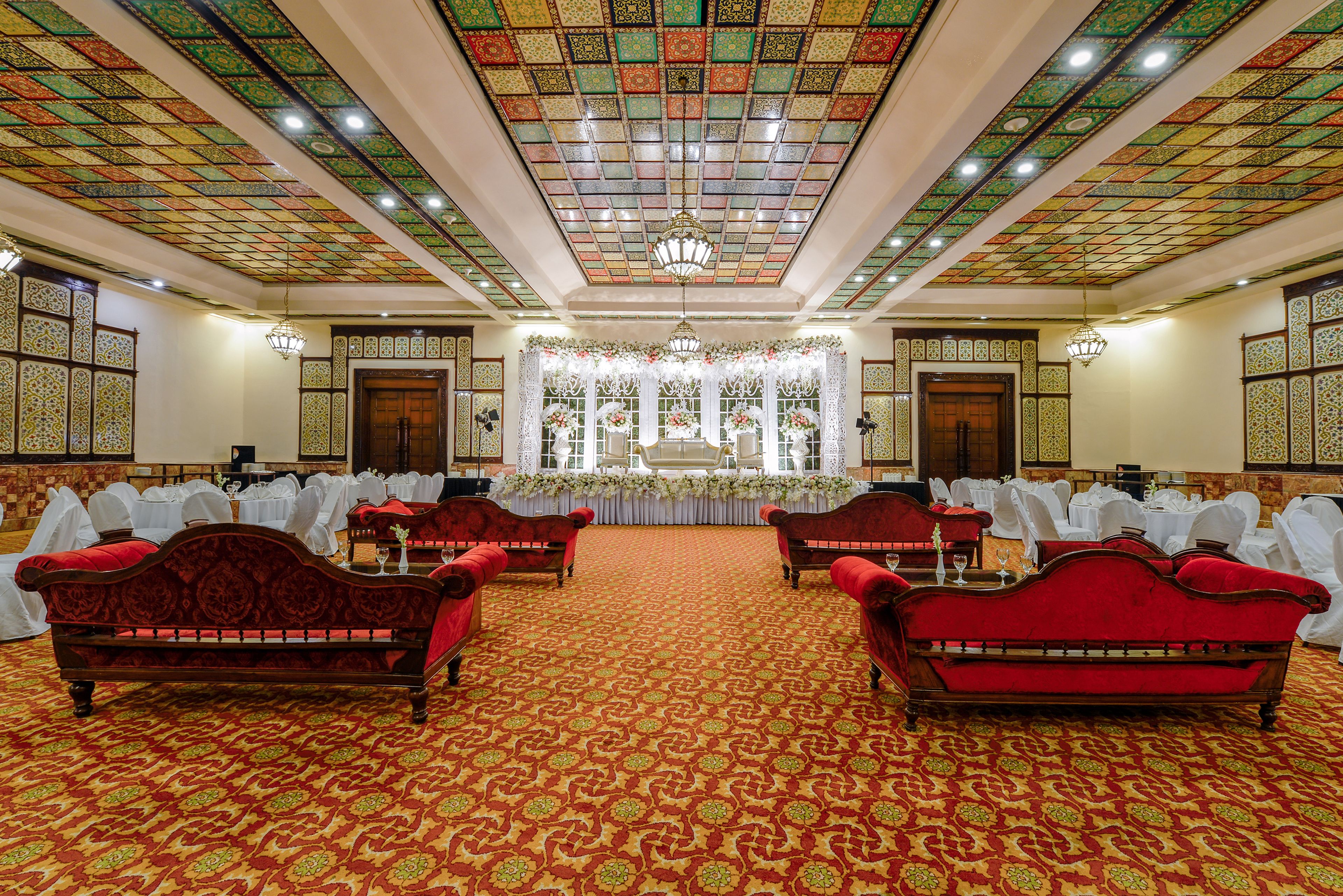 Un salón de banquetes con azulejos de techo ornamentados, sofás tapizados en rojo y un arreglo floral en la parte delantera.