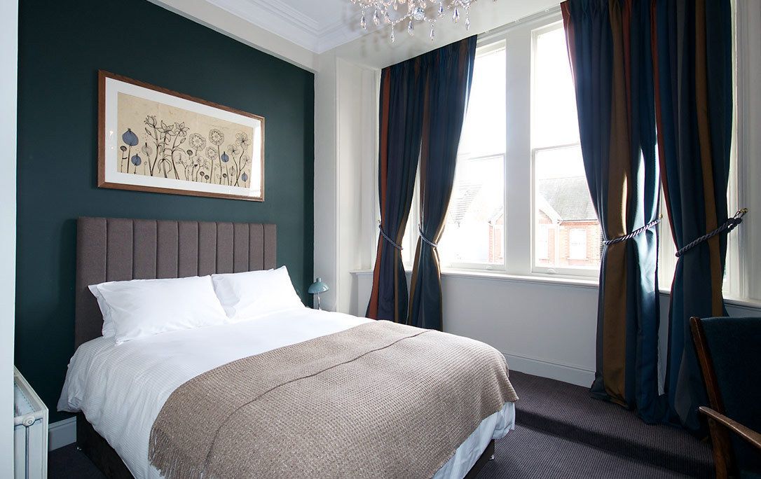 A neatly made bed with a headboard, a framed artwork on the wall, and a window with curtains.