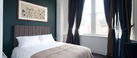 A neatly made bed with a headboard, a framed artwork on the wall, and a window with curtains.