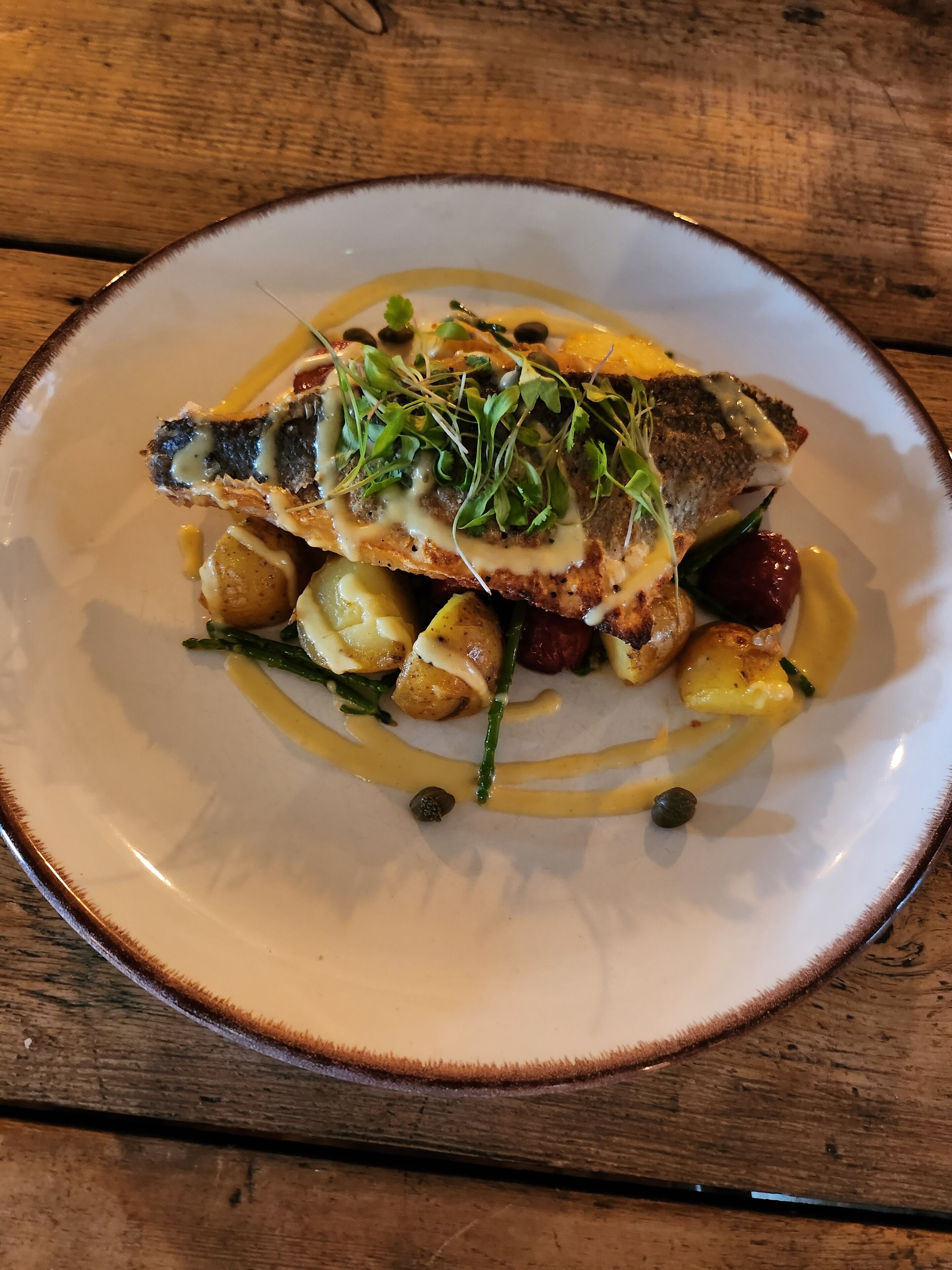 A plate of food with a piece of fish, potatoes, and greens.
