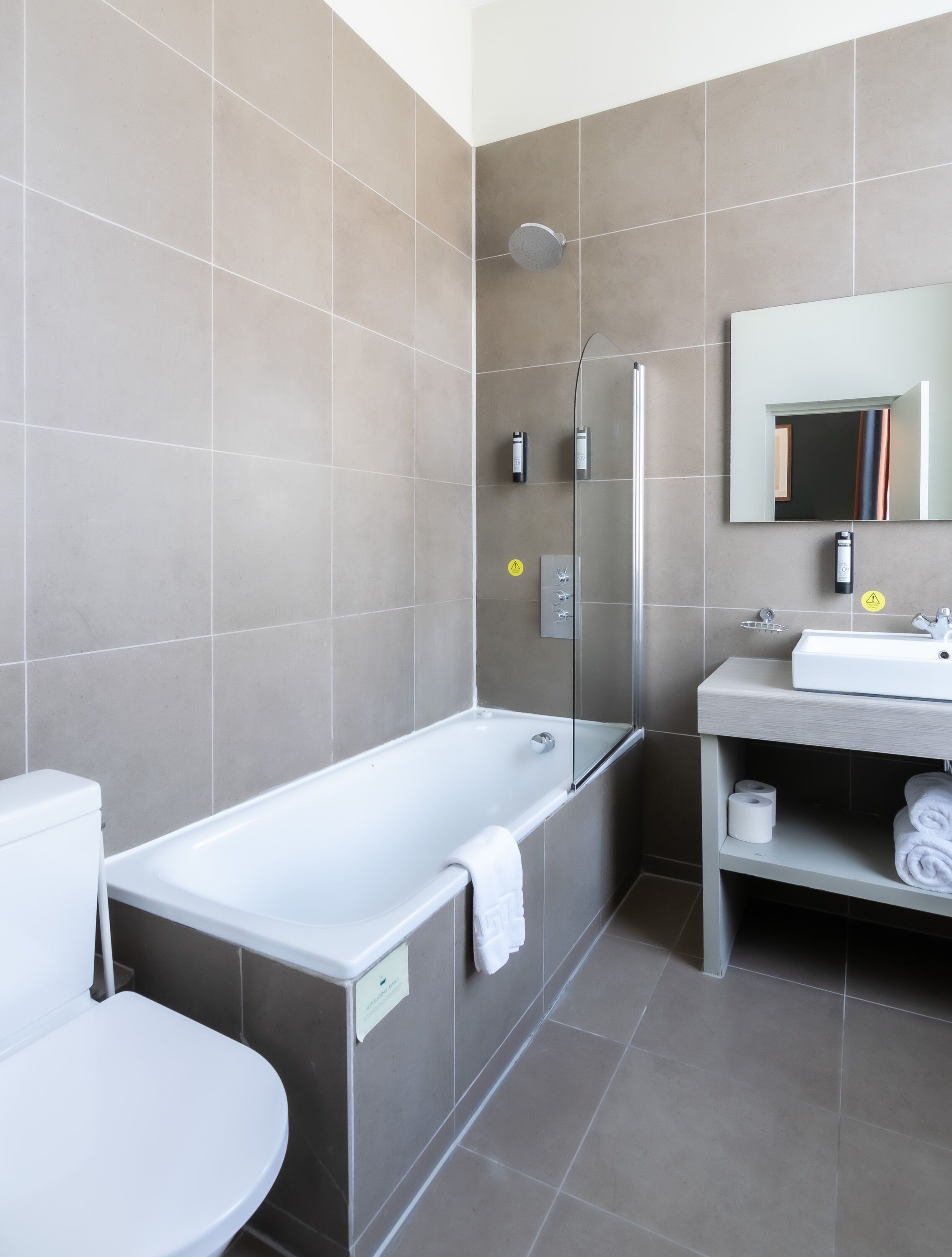 A modern bathroom with a glass-enclosed shower, a white bathtub, a sink with a mirror, and a toilet.
