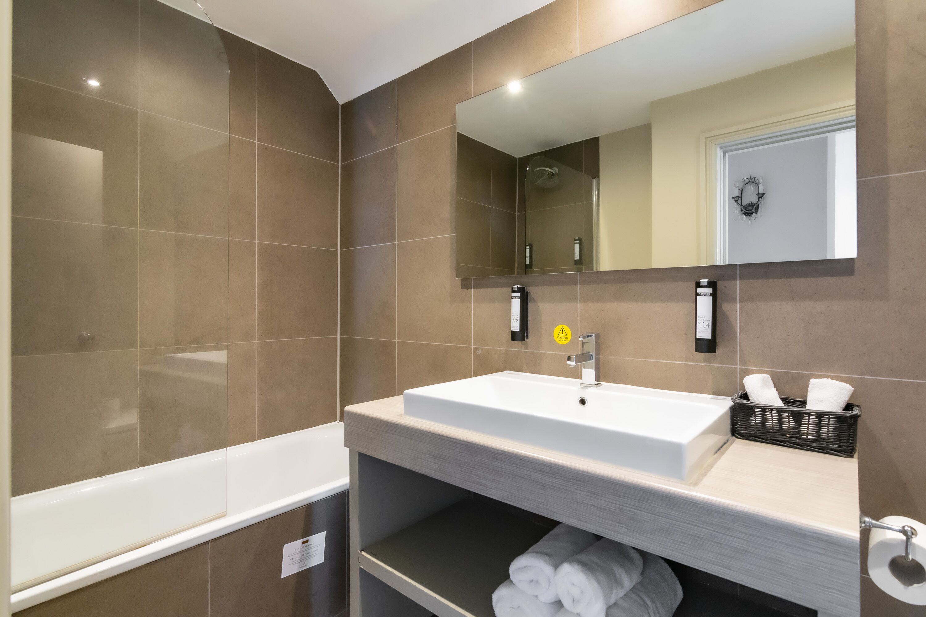 A modern bathroom with a large bathtub, a sink with a mirror, and a shelf with towels.