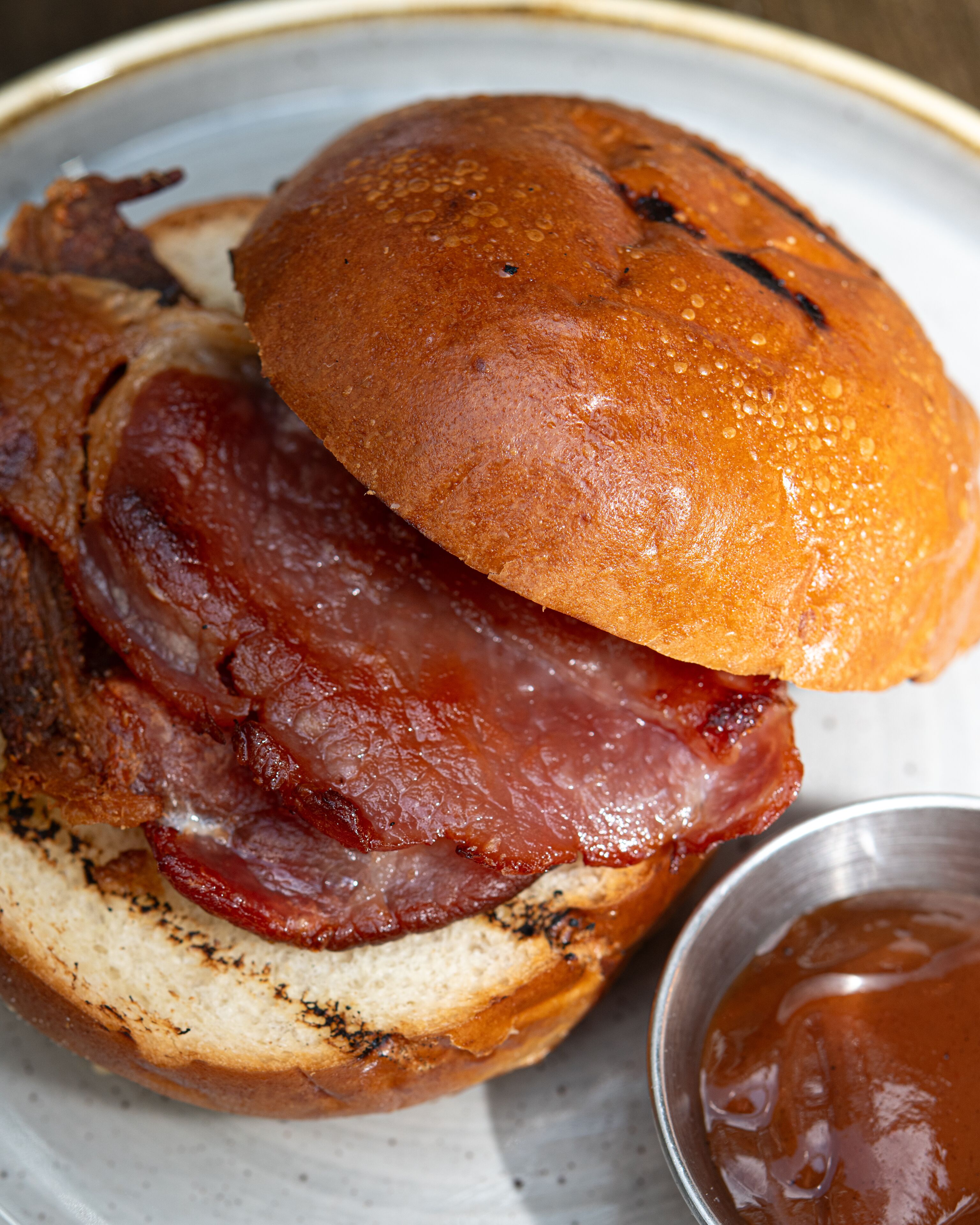 Un sandwich servi dans un pain, avec du bacon et accompagné d’une sauce.