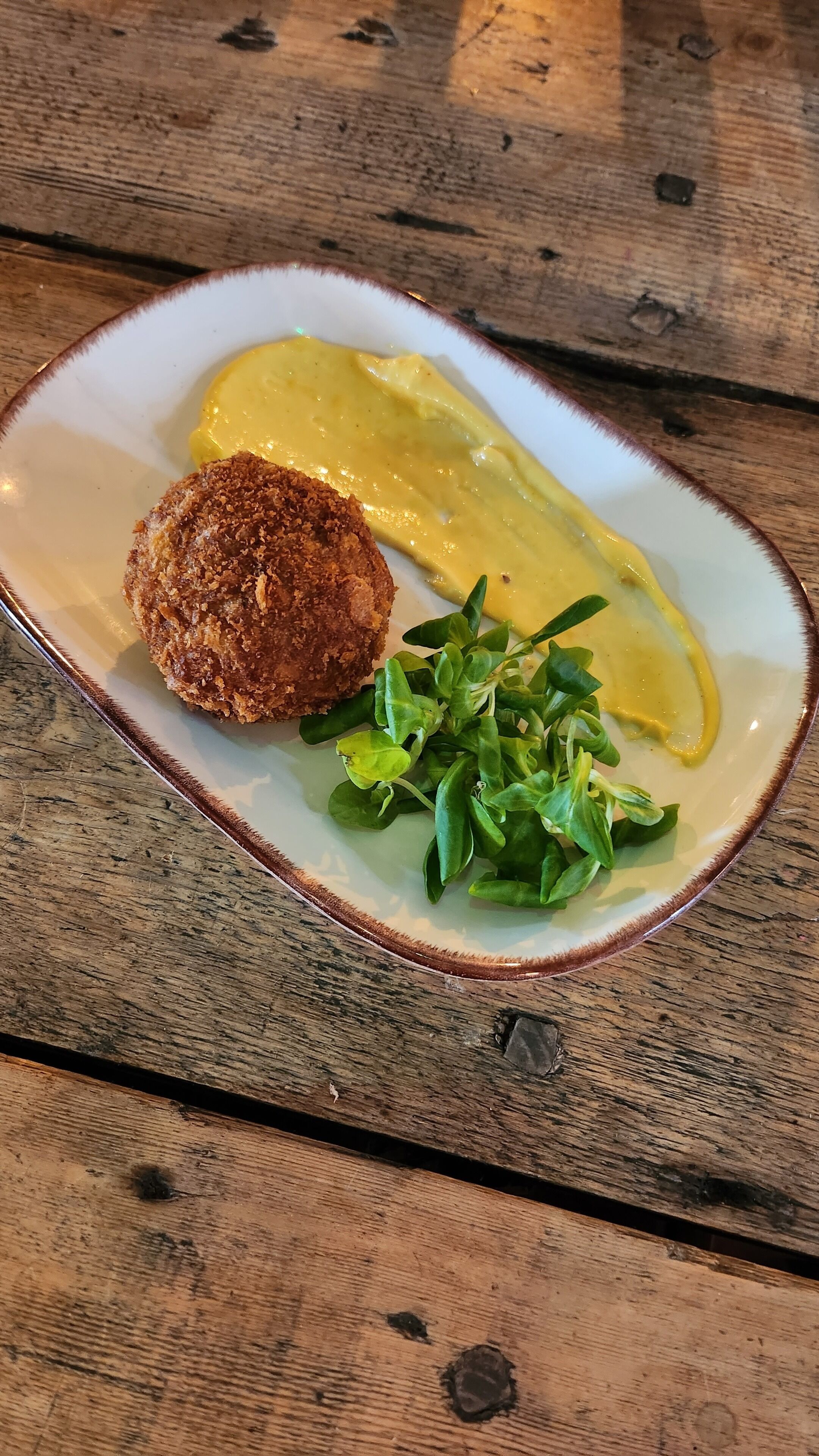 Un plat amb un aliment rebrut, una salsa groga i fulles verdes damunt d'una taula de fusta.
