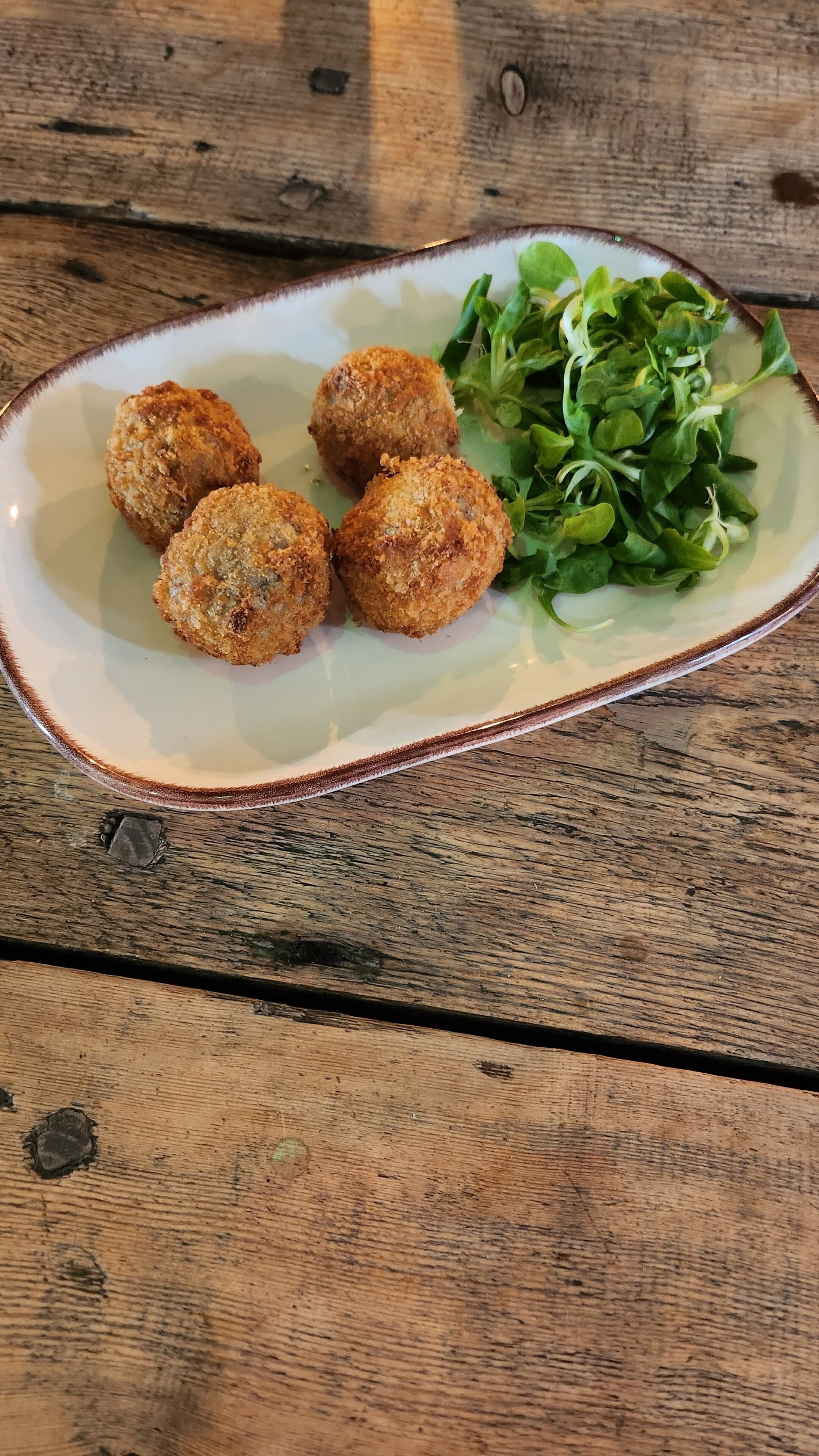 Een bord met vier gebakken balletjes en een portie groen op een houten tafel.