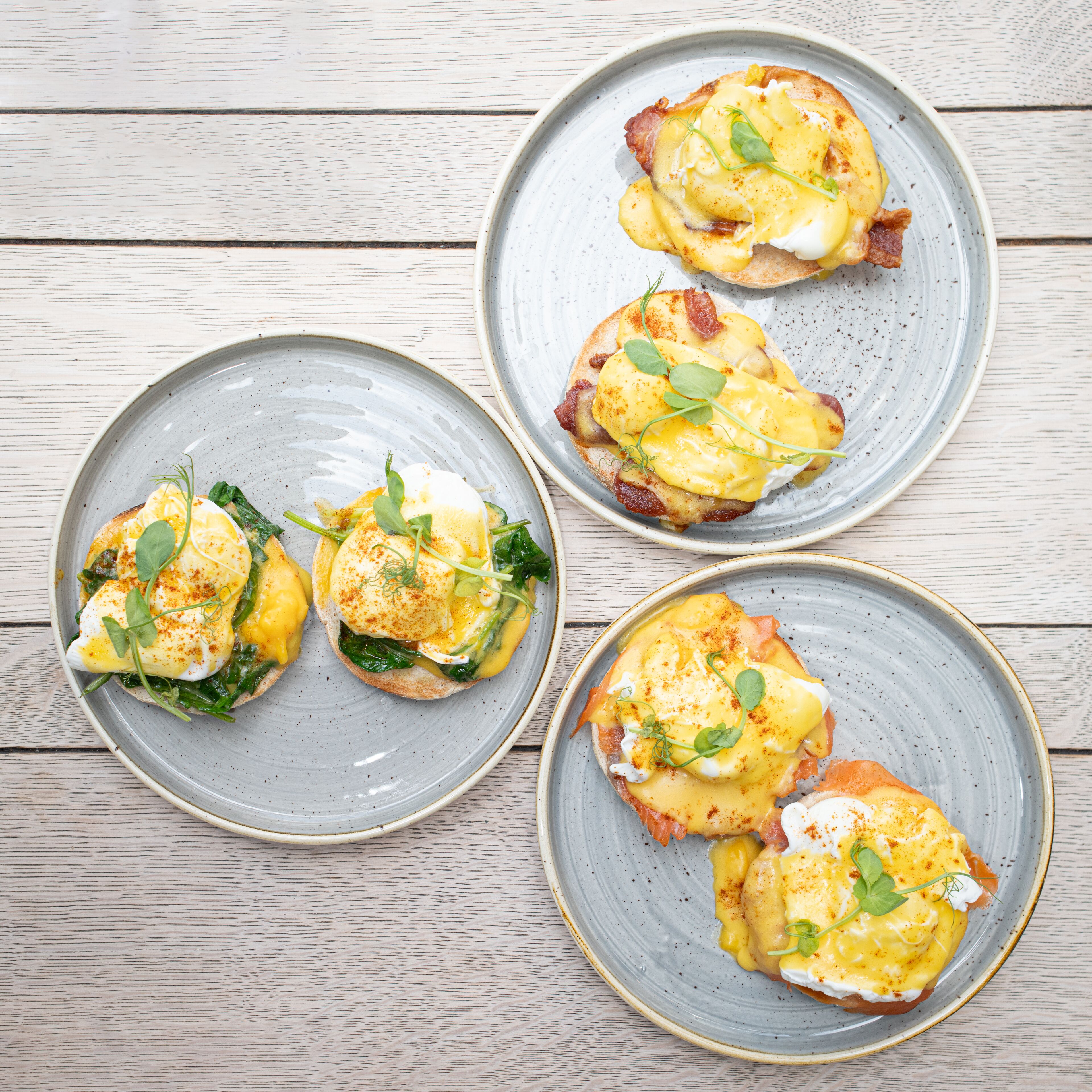 Trois assiettes d’œufs Bénédicte sur une table en bois.