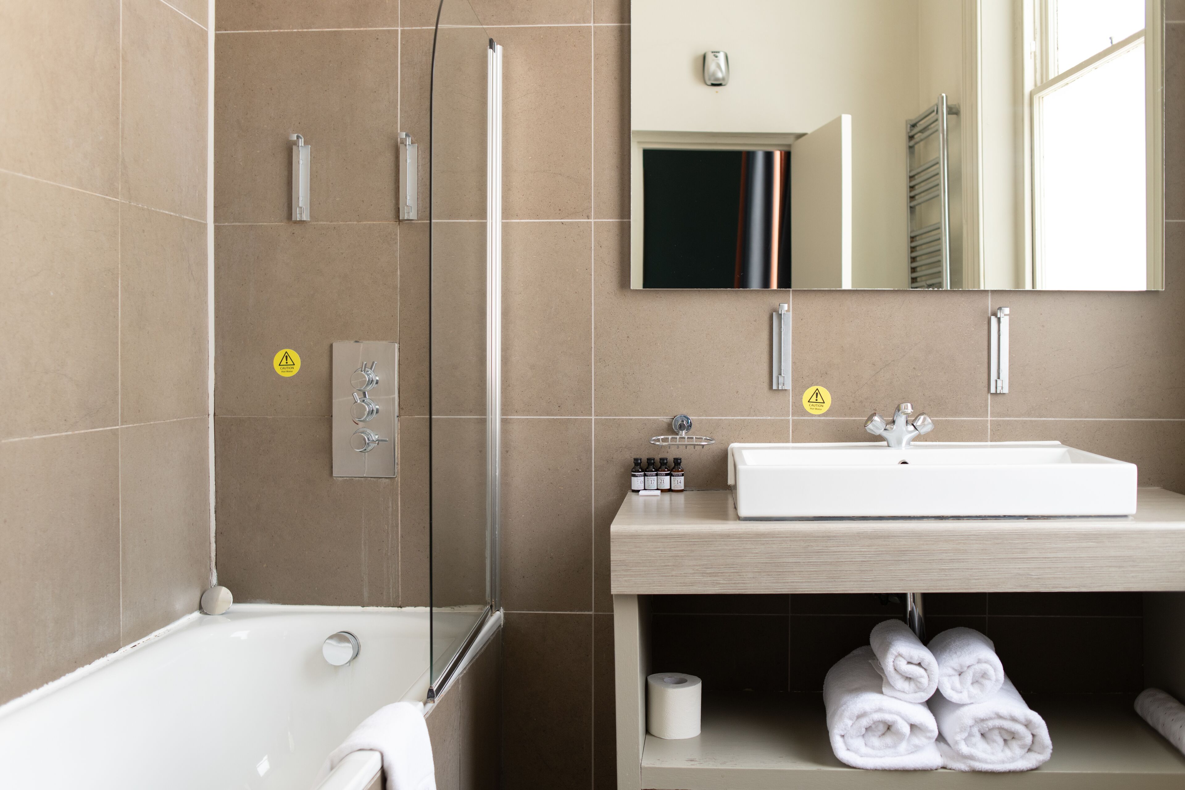 A modern bathroom with a bathtub, a glass shower enclosure, a sink with a mirror, and neatly rolled towels on a shelf.