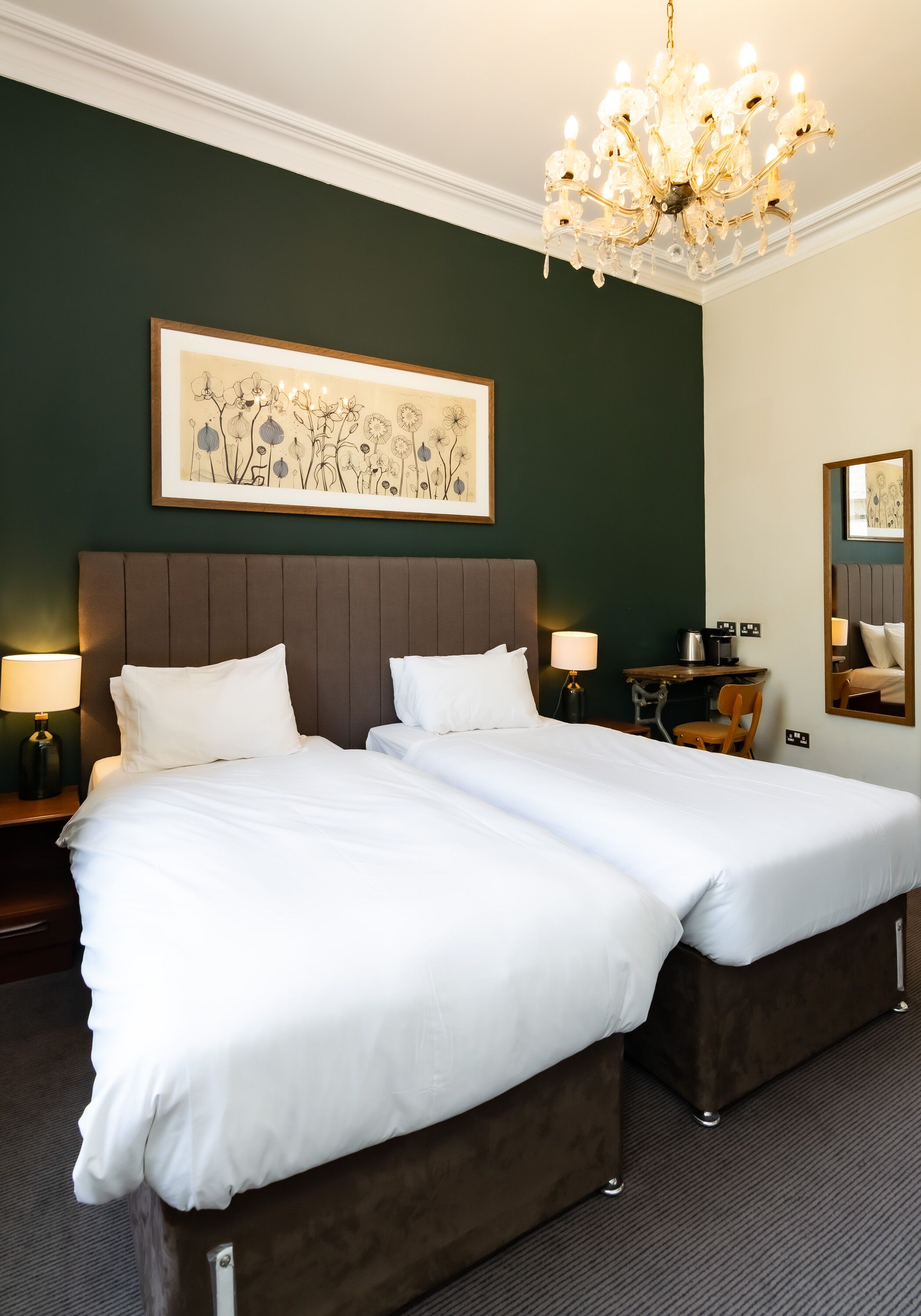 A double bed with white linens, a dark headboard, and a chandelier.