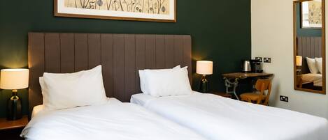 A double bed with white linens, a dark headboard, and a chandelier.