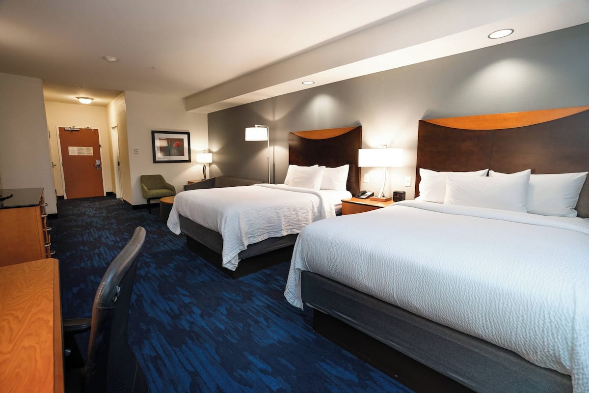 A hotel room with two beds, a desk, a chair, and a door.