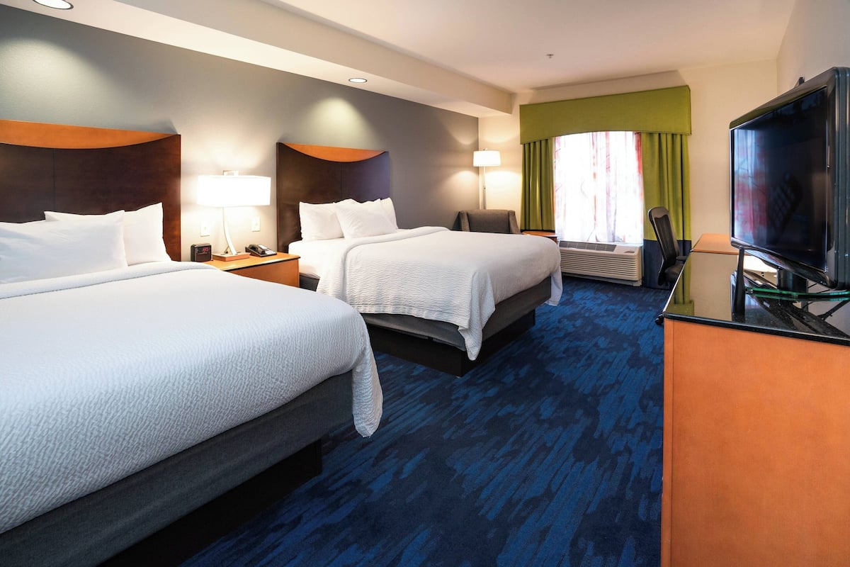 A hotel room with two beds, a desk with a television, and a window with curtains.
