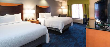 A hotel room with two beds, a desk with a television, and a window with curtains.