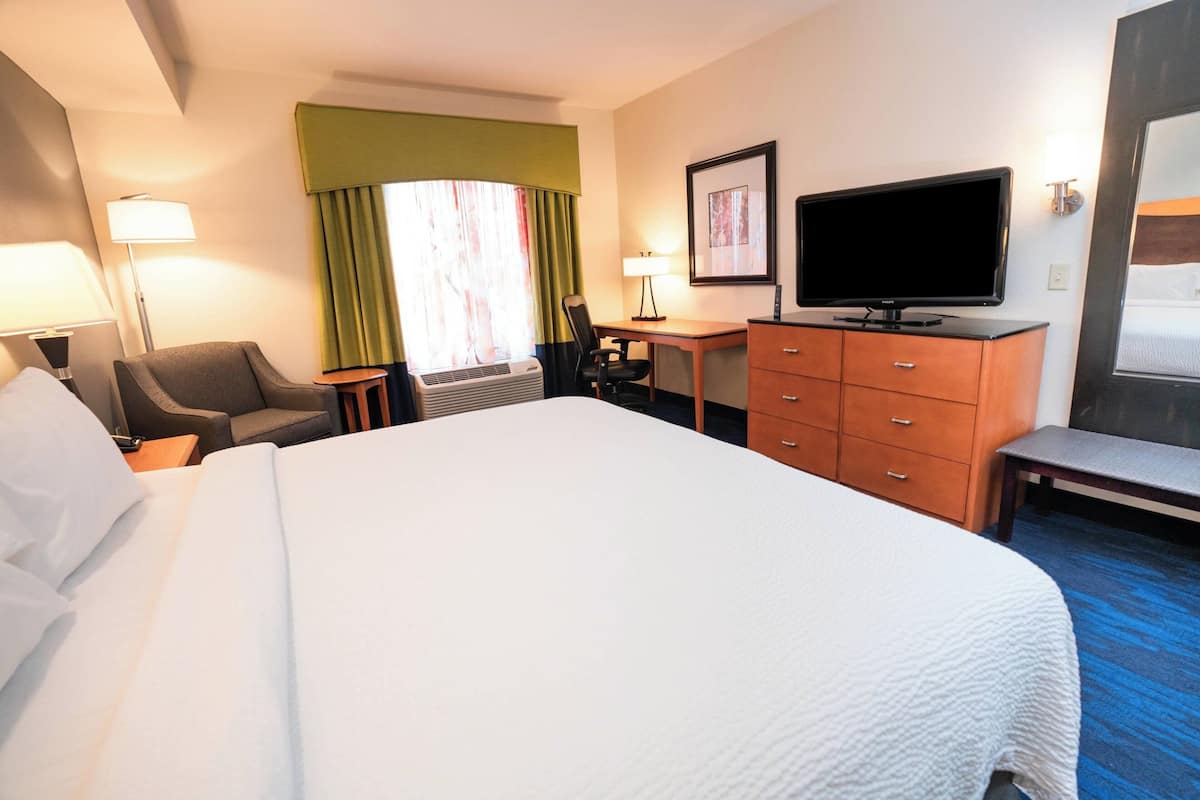 A hotel room with a large bed, a desk with a computer, a television, and a chair.