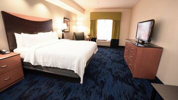 A hotel room with a large bed, a desk with a computer, a chair, a dresser, and a television.