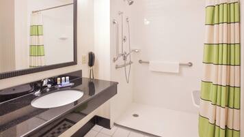 Une salle de bain avec un lavabo à vasque et un plan de toilette noir, un miroir, une douche avec un rideau vert et un mur recouvert de carreaux blancs.