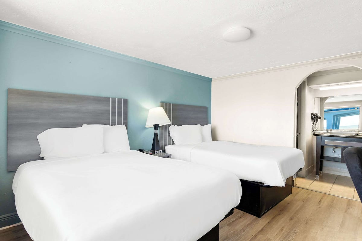 A hotel room with two beds, a desk, and a chair.