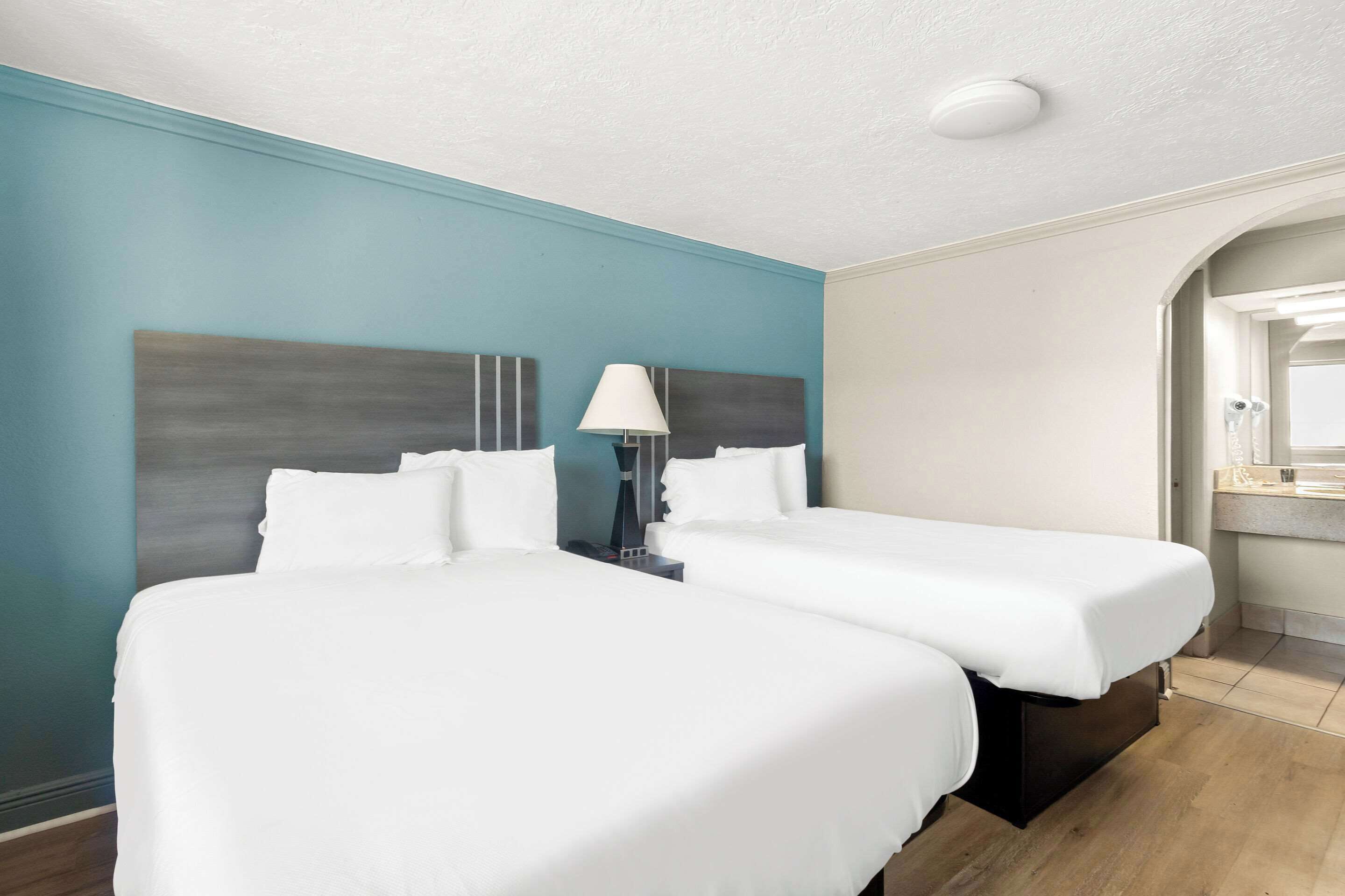 Une chambre d’hôtel avec deux lits, une table de chevet avec une lampe et une salle de bain visible à travers une arche.