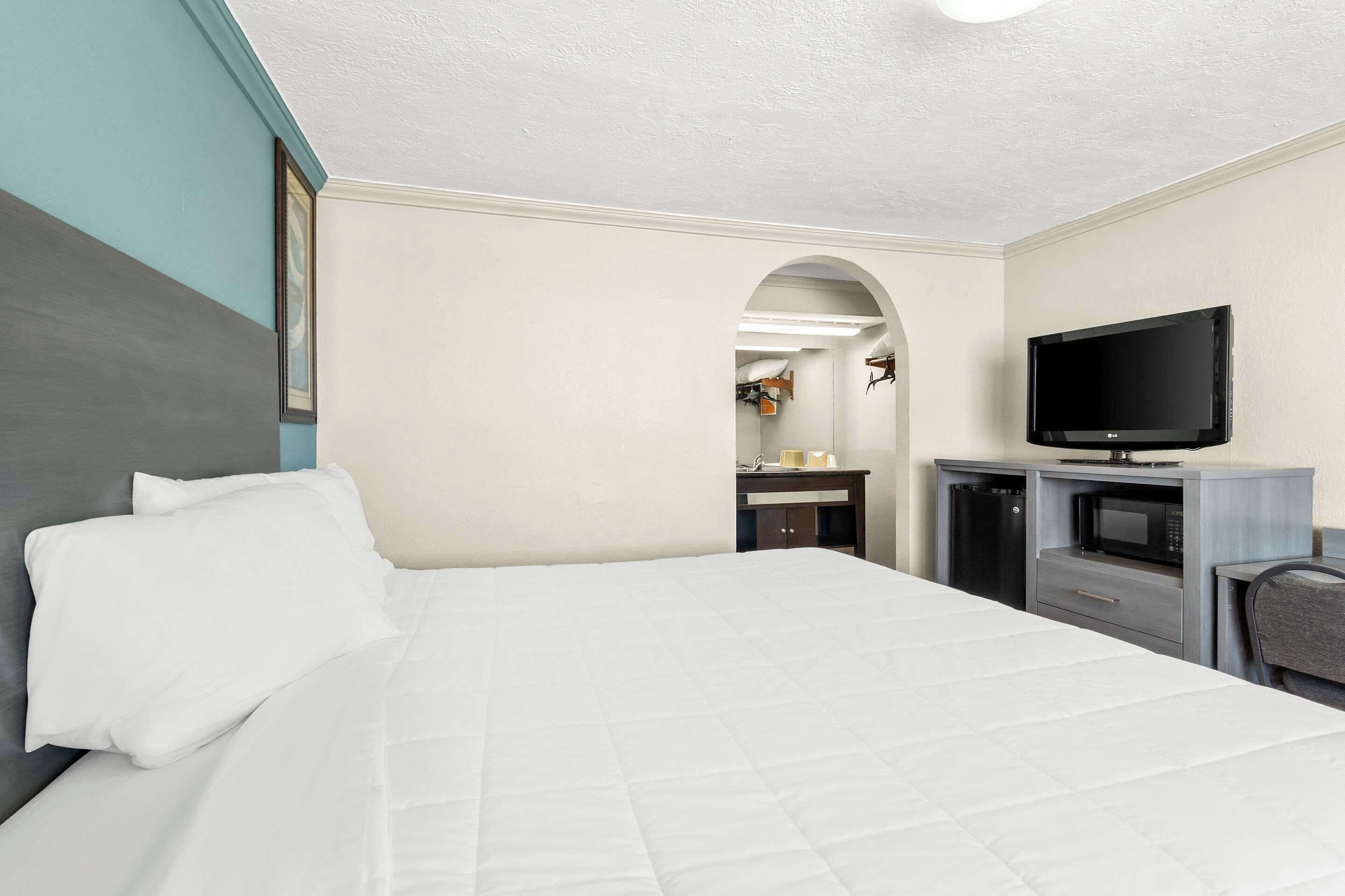 Une chambre d’hôtel équipée d’un lit, d’une télévision, d’un bureau avec un micro-ondes et d’une petite kitchenette.