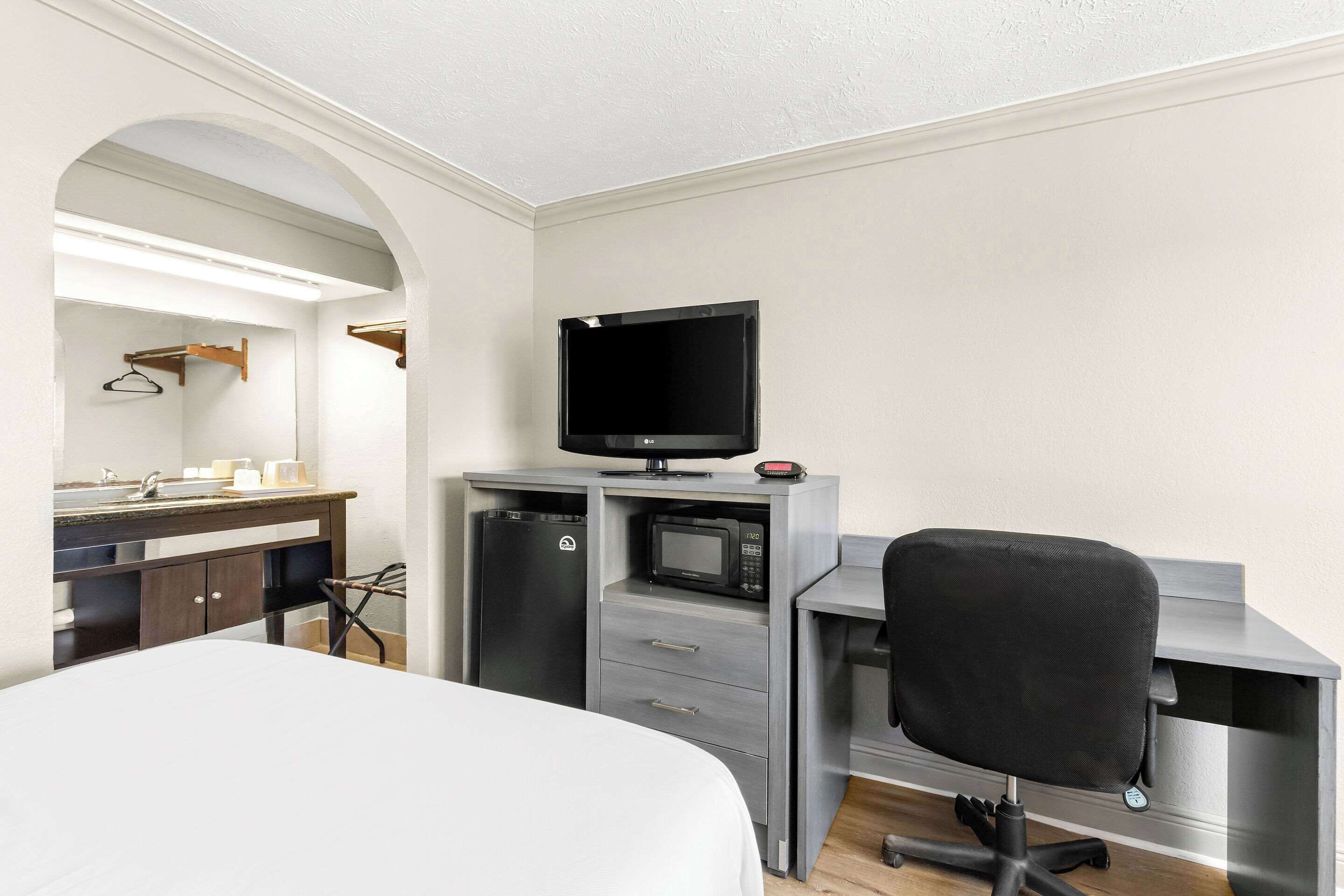 Habitación de hotel con cama, escritorio con computadora, televisor y microondas.