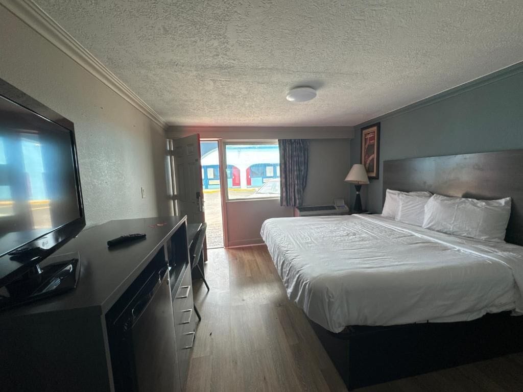 A hotel room with a bed, a TV, a desk, and a window with a view of a building.
