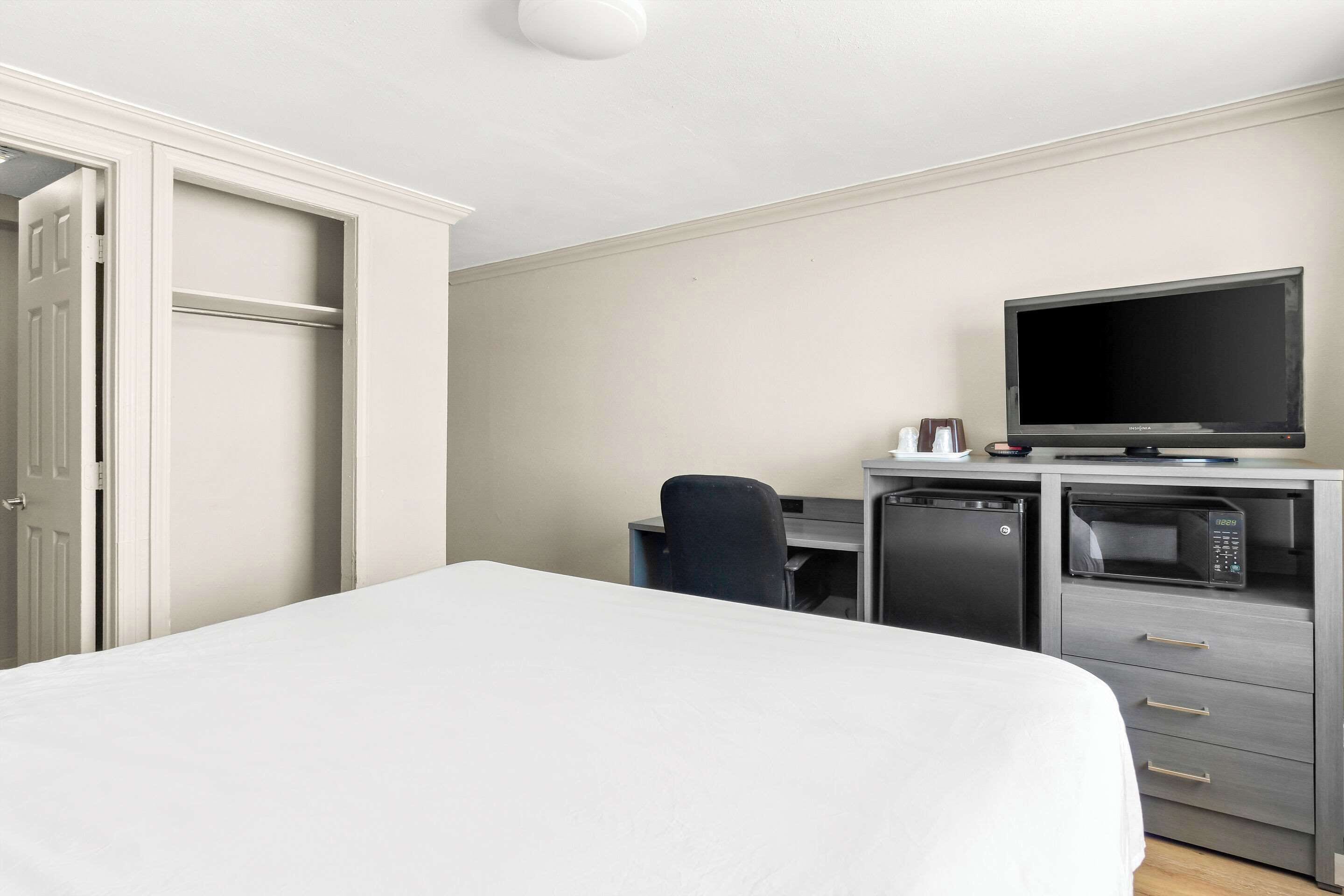 A hotel room with a bed, a desk with a computer, a television, and a microwave.