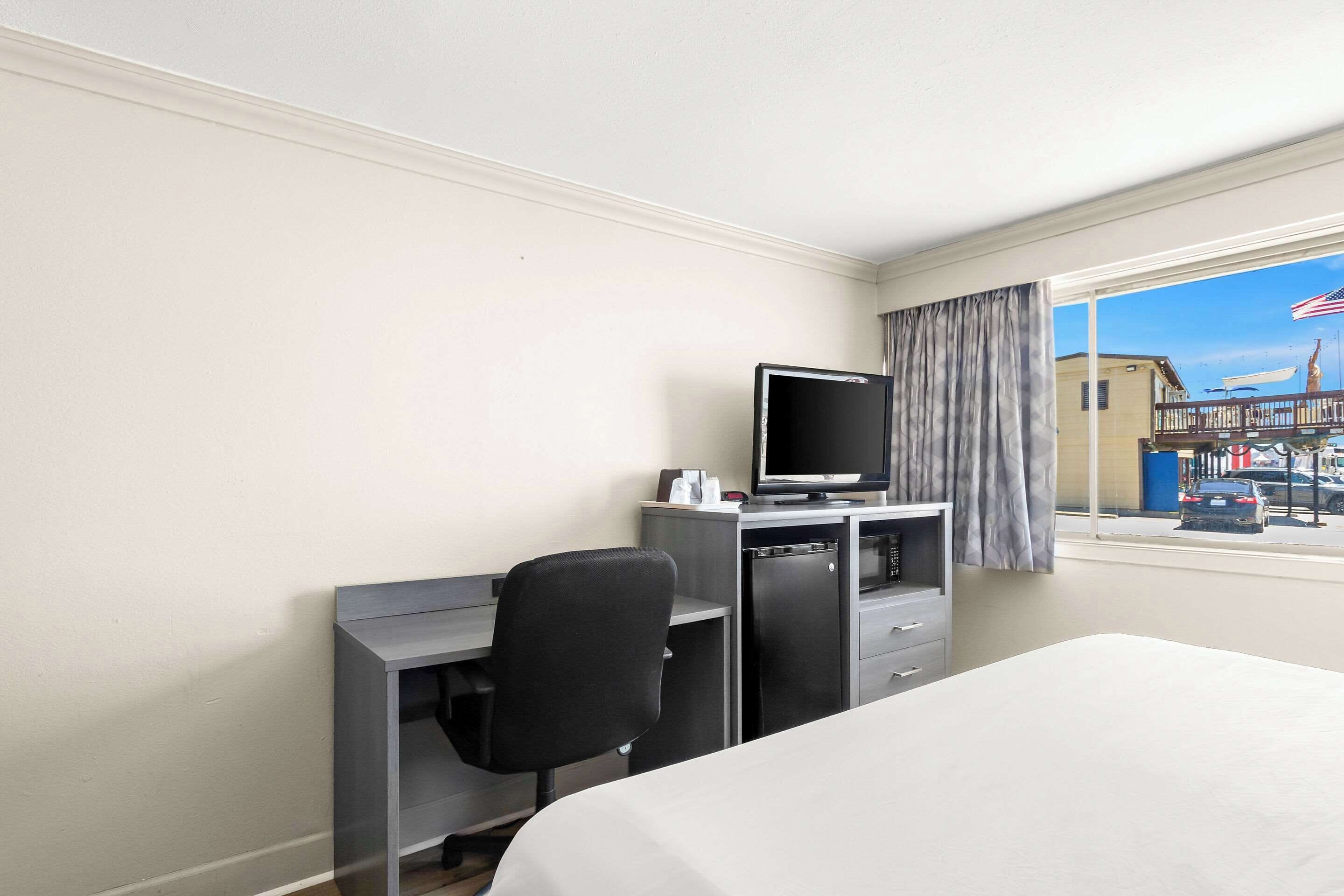 Une chambre d’hôtel avec un lit, un bureau équipé d’un ordinateur et une fenêtre donnant sur une rue et des immeubles.