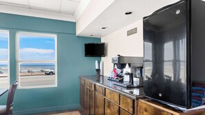 Un área de cocina con refrigerador, cafetera y televisión en la pared.