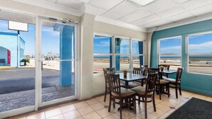 Un restaurante con vista a la playa, que cuenta con un comedor con mesas y sillas, ventanas amplias y una pared de acento azul.