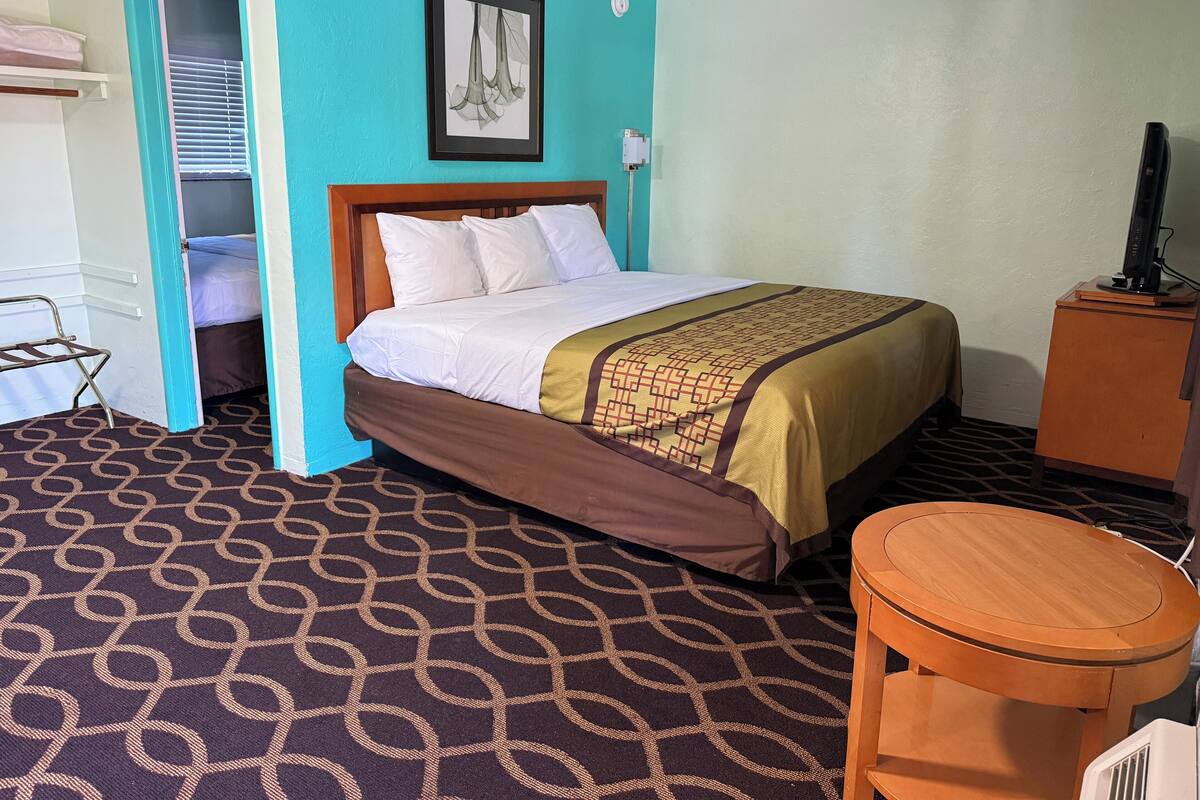 A hotel room with a bed, a desk, a chair, a wardrobe, and a picture on the wall.